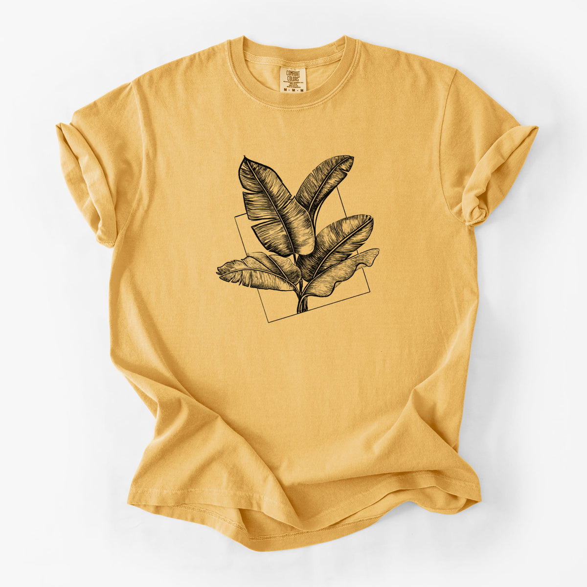 Golden wheat yellow Comfort Colors t-shirt laid flat, printed with a black ink illustration of banana leaves in front of a square outline.