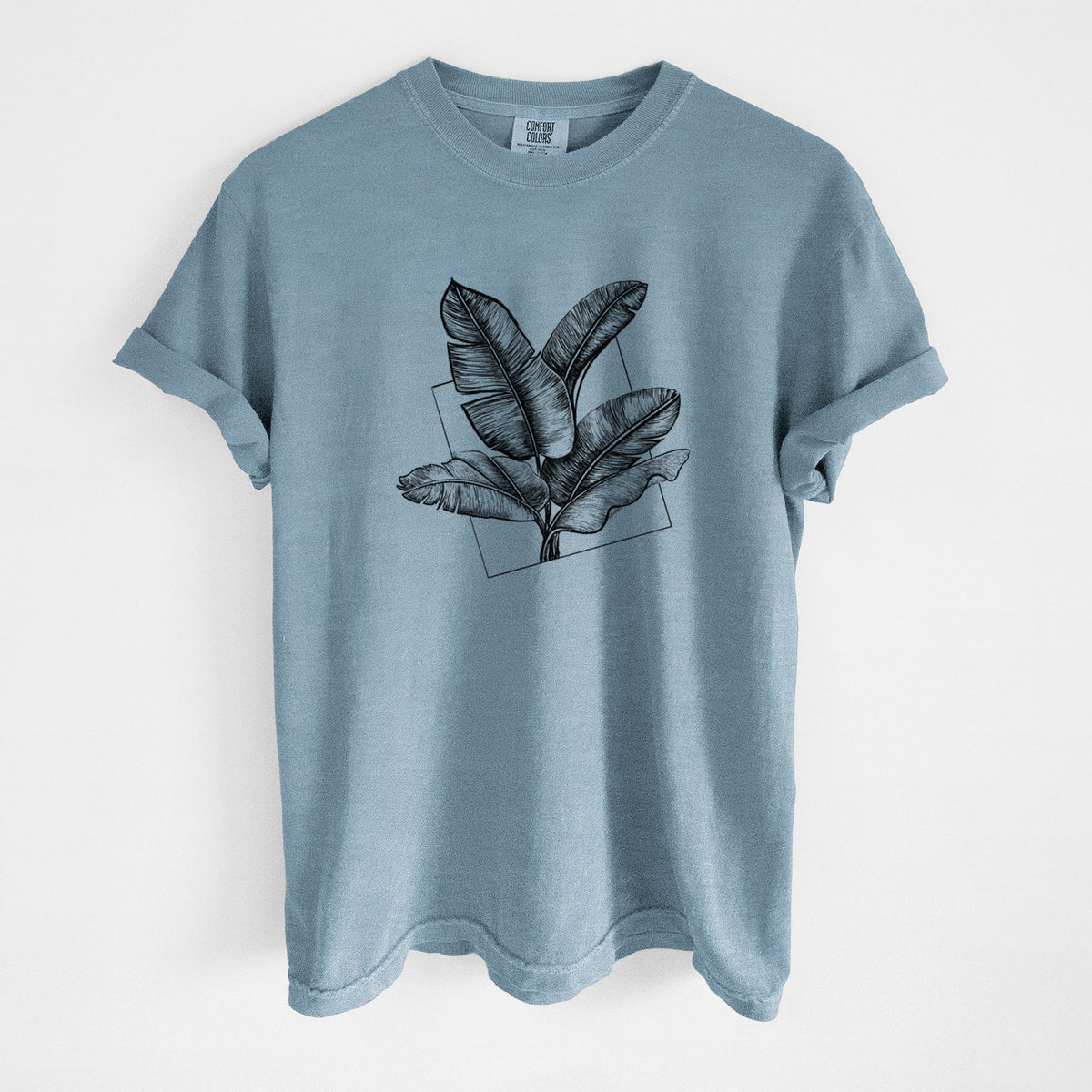 Steel blue Comfort Colors t-shirt laid flat, printed with a black ink illustration of banana leaves in front of a square outline.