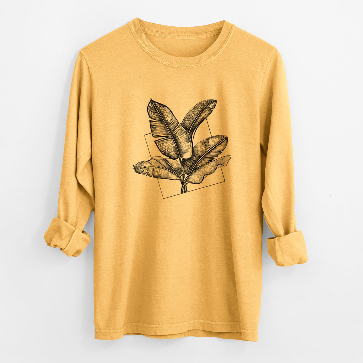 Golden wheat yellow Comfort Colors long sleeve shirt laid flat with the cuffs rolled, printed with a black ink illustration of banana leaves in front of a square outline.