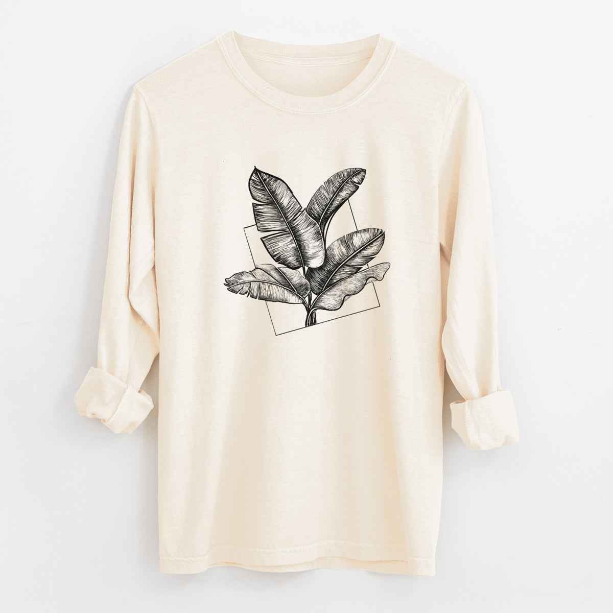 Ivory Comfort Colors long sleeve shirt laid flat with the cuffs rolled, printed with a black ink illustration of banana leaves in front of a square outline.