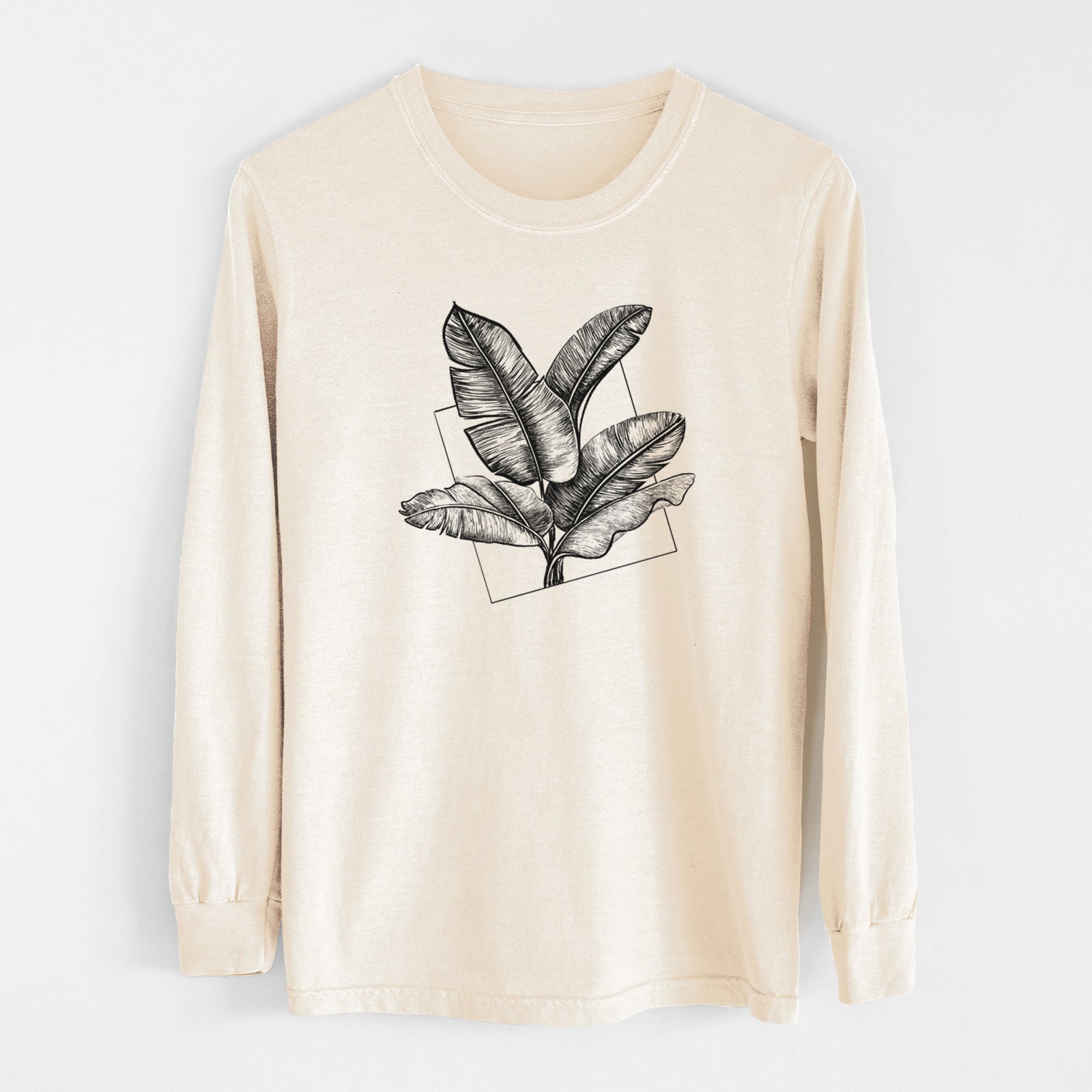Ivory Comfort Colors long sleeve shirt laid flat, printed with a black ink illustration of banana leaves in front of a square outline.