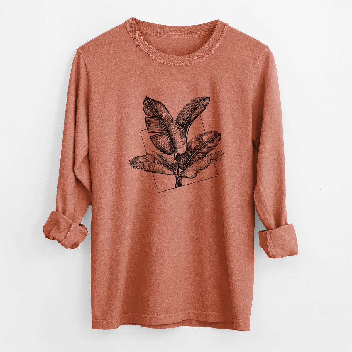 Yam burnt orange Comfort Colors long sleeve shirt laid flat with the cuffs rolled, printed with a black ink illustration of banana leaves in front of a square outline.