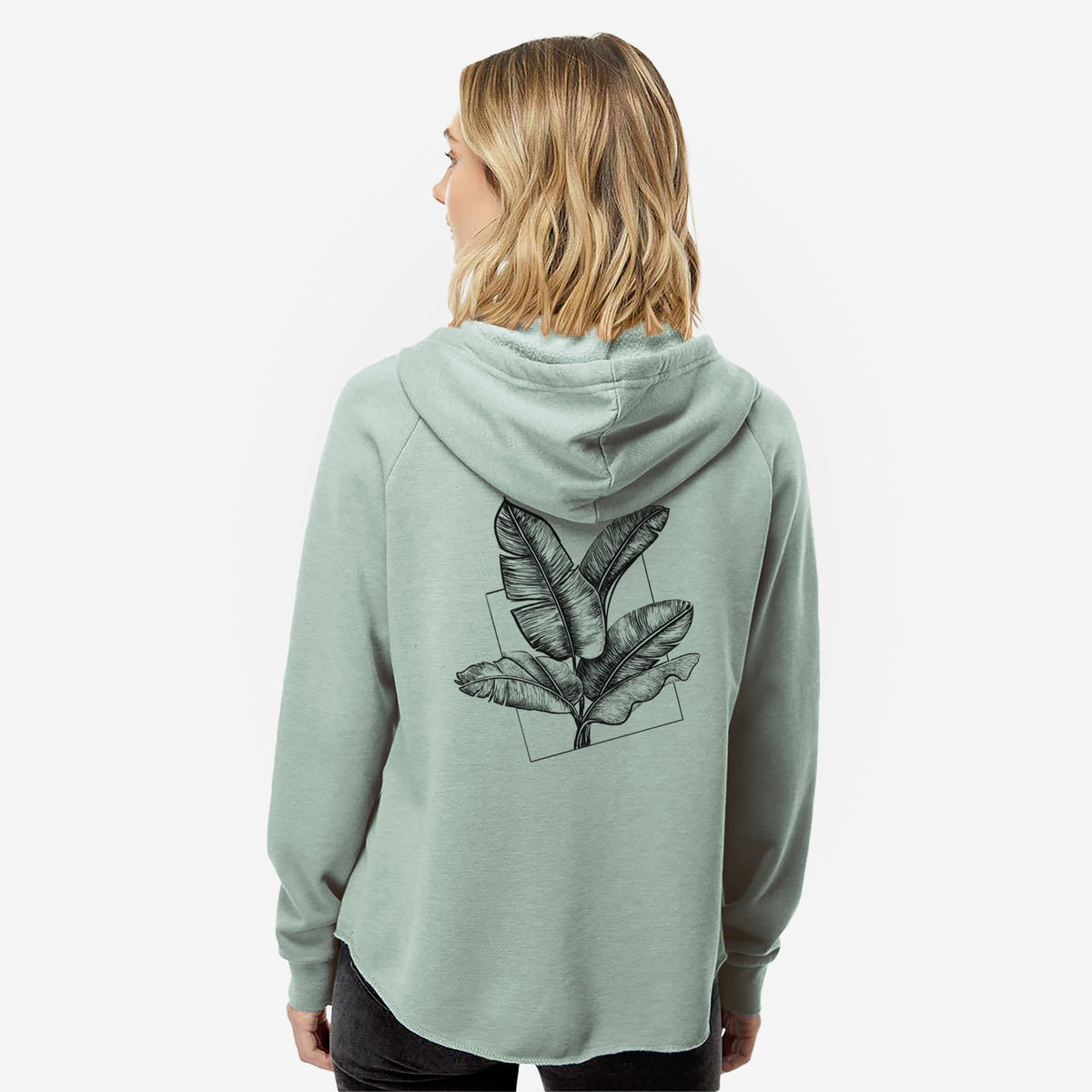 Woman wearing a sage green women's Cali Wave zip-up sweatshirt printed with a black ink illustration of banana leaves in front of a square outline, seen from behind.