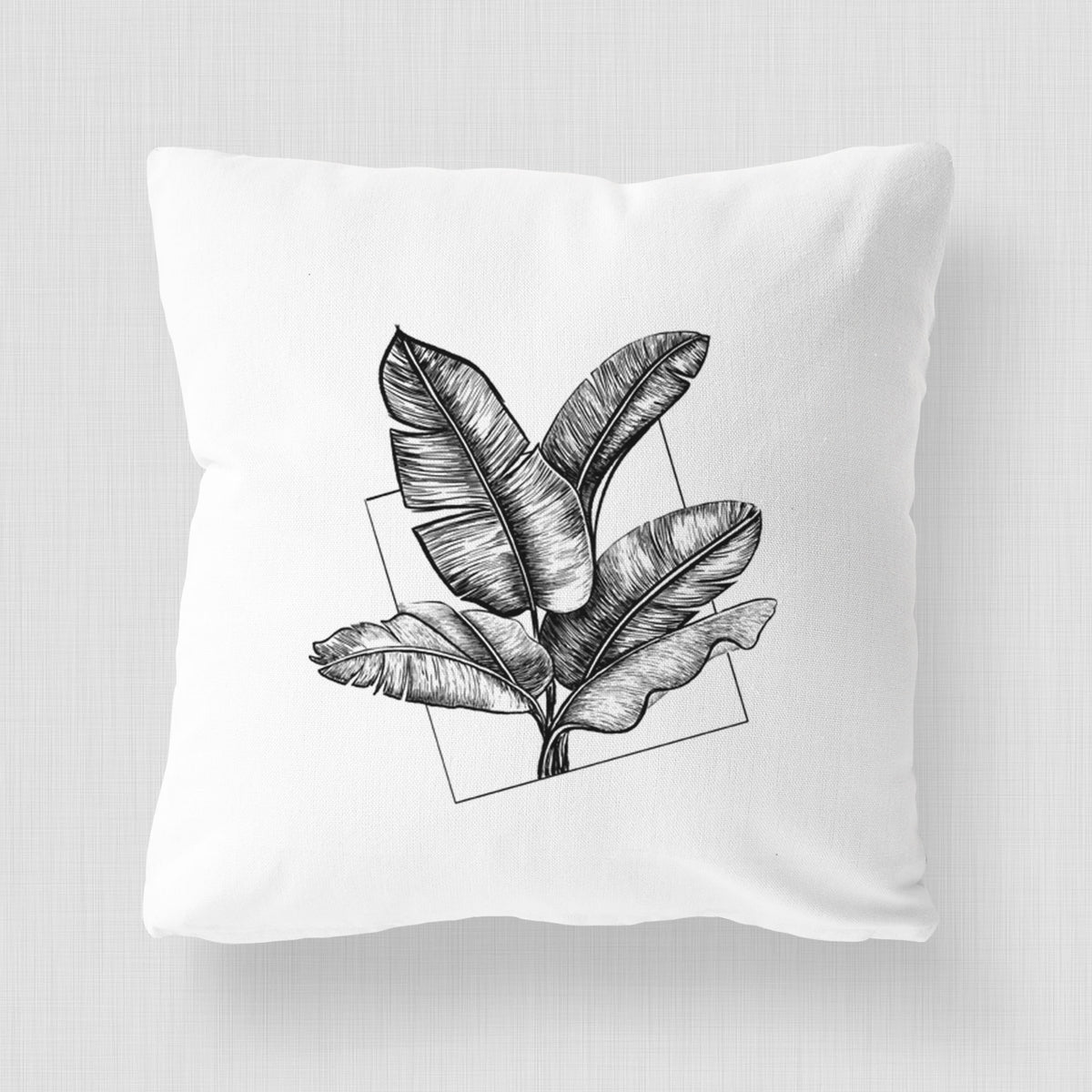 White pillow cover printed with a black ink illustration of banana leaves in front of a square outline.