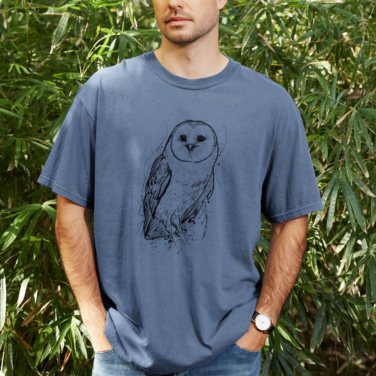 Man wearing a Comfort Colors t-shirt printed with a detailed black ink illustration of a barn owl standing and facing forward, outdoors.