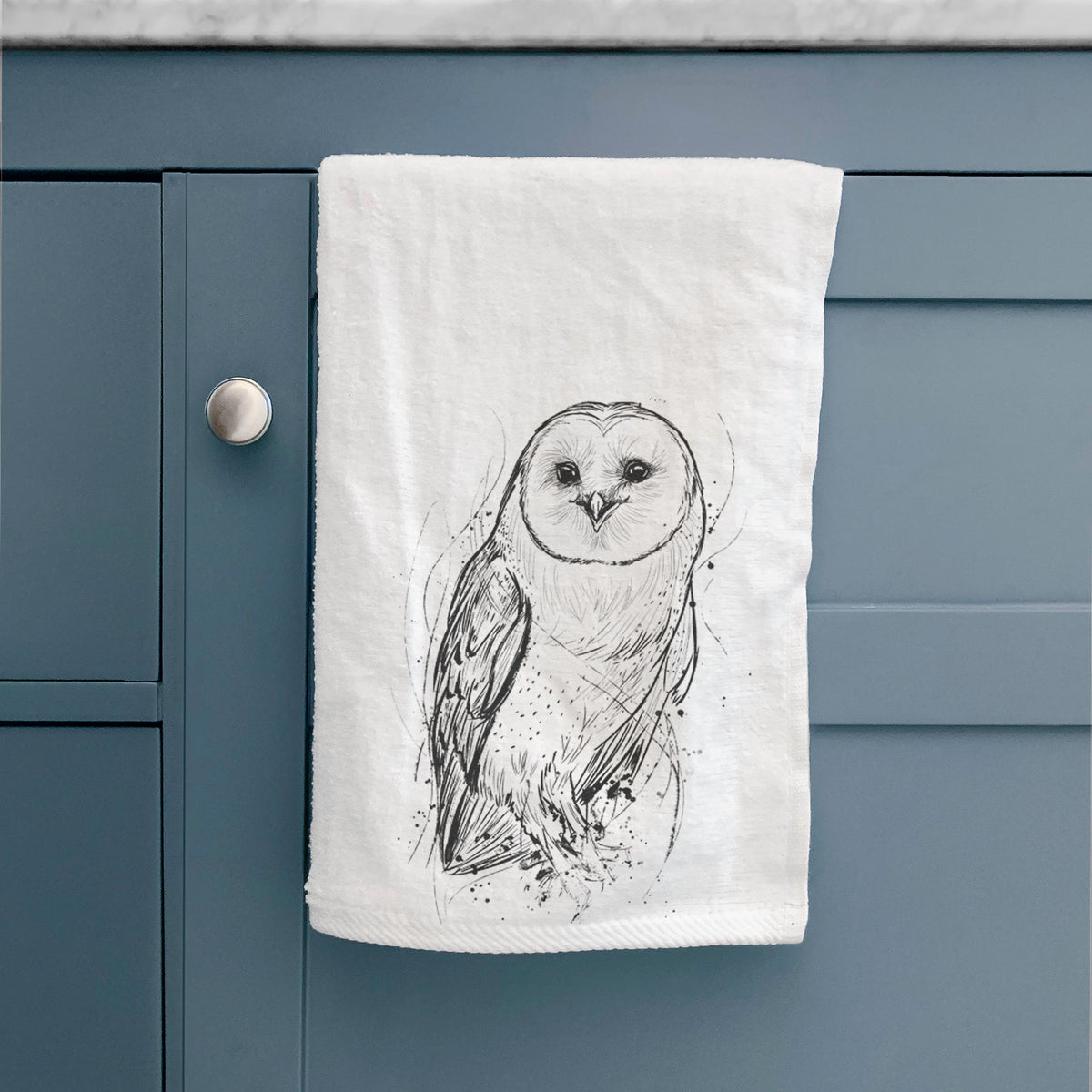 White hand towel printed with a detailed black ink illustration of a barn owl standing and facing forward, hanging on a cabinet door.