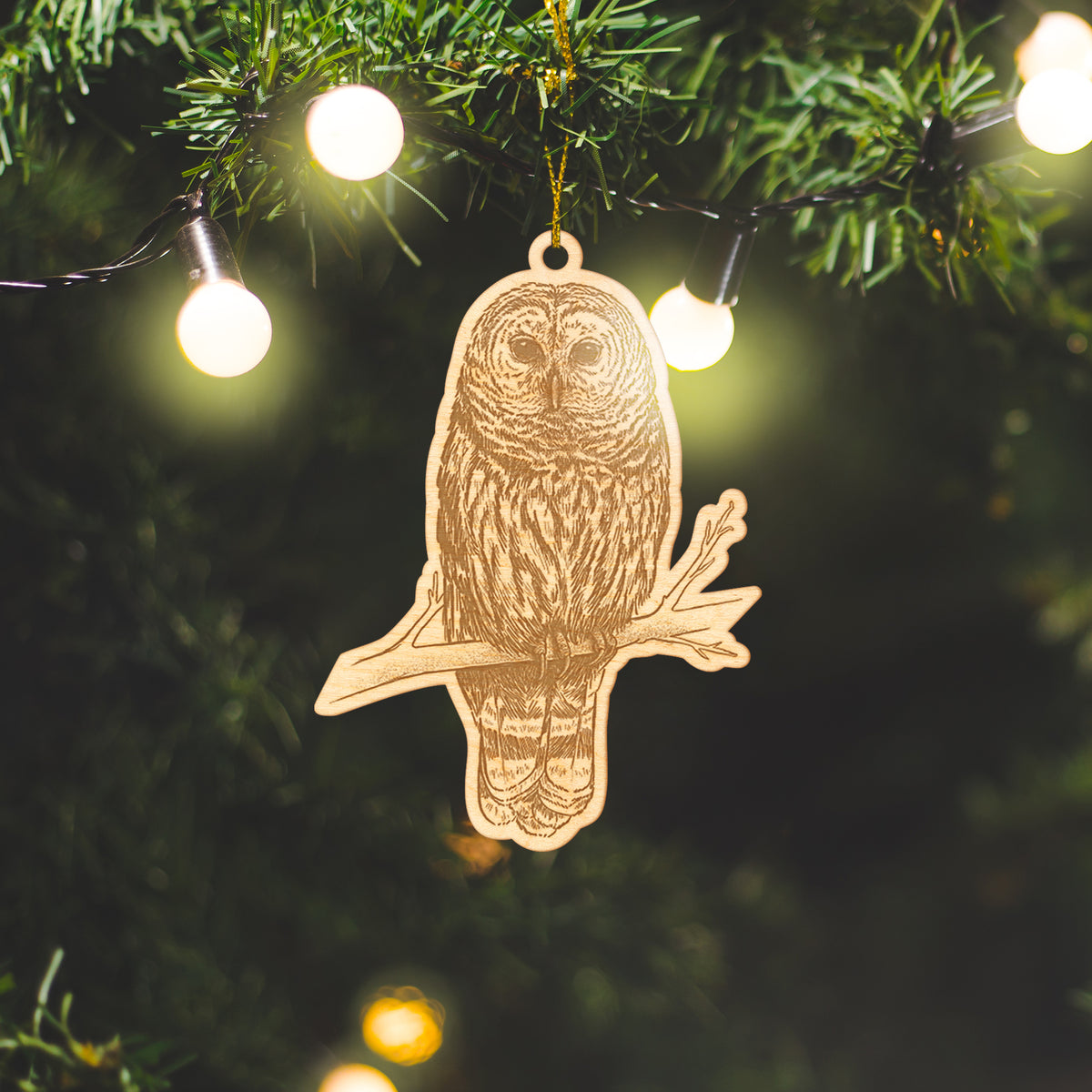 Wooden ornament featuring a detailed engraving of a barred owl perched on a branch, on a knit blanket with pine cones.