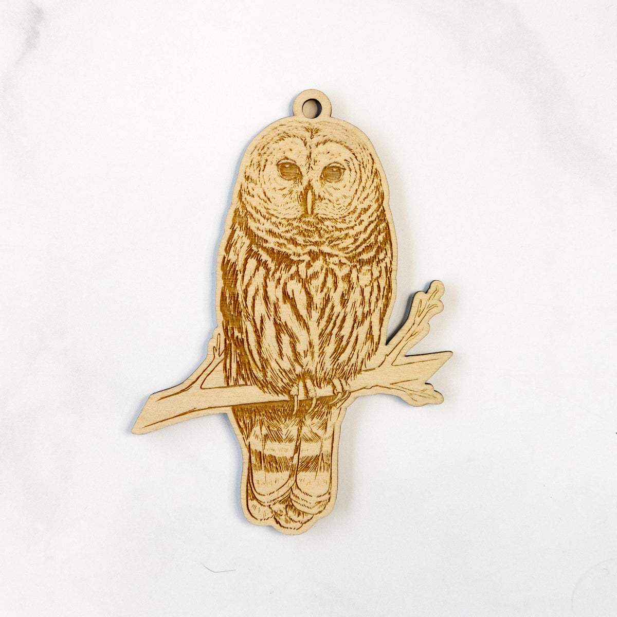 Wooden ornament featuring a detailed engraving of a barred owl perched on a branch, on a marble surface.