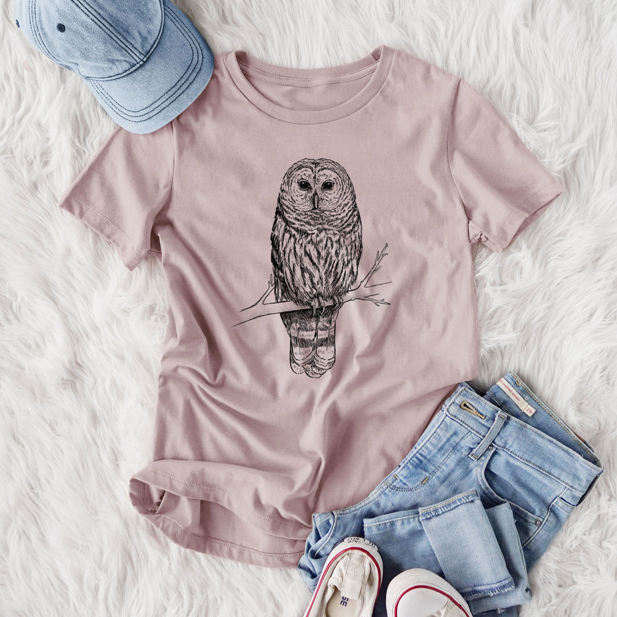 Women's relaxed fit cotton t-shirt printed with a detailed black ink illustration of a barred owl perched on a branch, styled flat on a white faux fur rug with jeans.