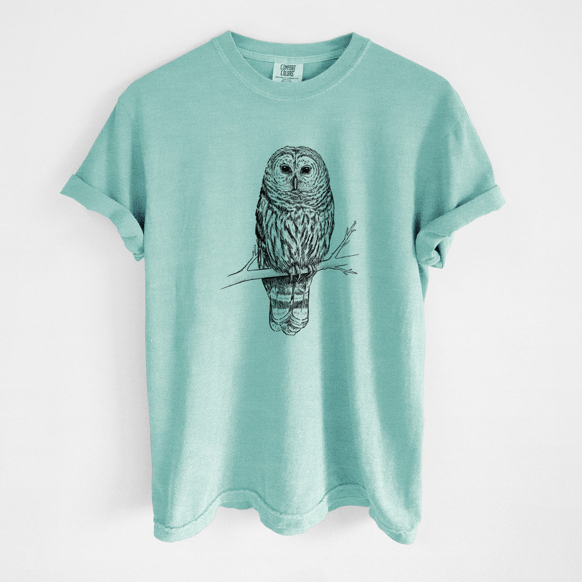 Chalky mint Comfort Colors t-shirt laid flat, printed with a detailed black ink illustration of a barred owl perched on a branch.