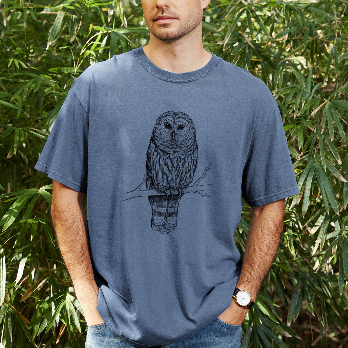 Man wearing a Comfort Colors t-shirt printed with a detailed black ink illustration of a barred owl perched on a branch, outdoors.