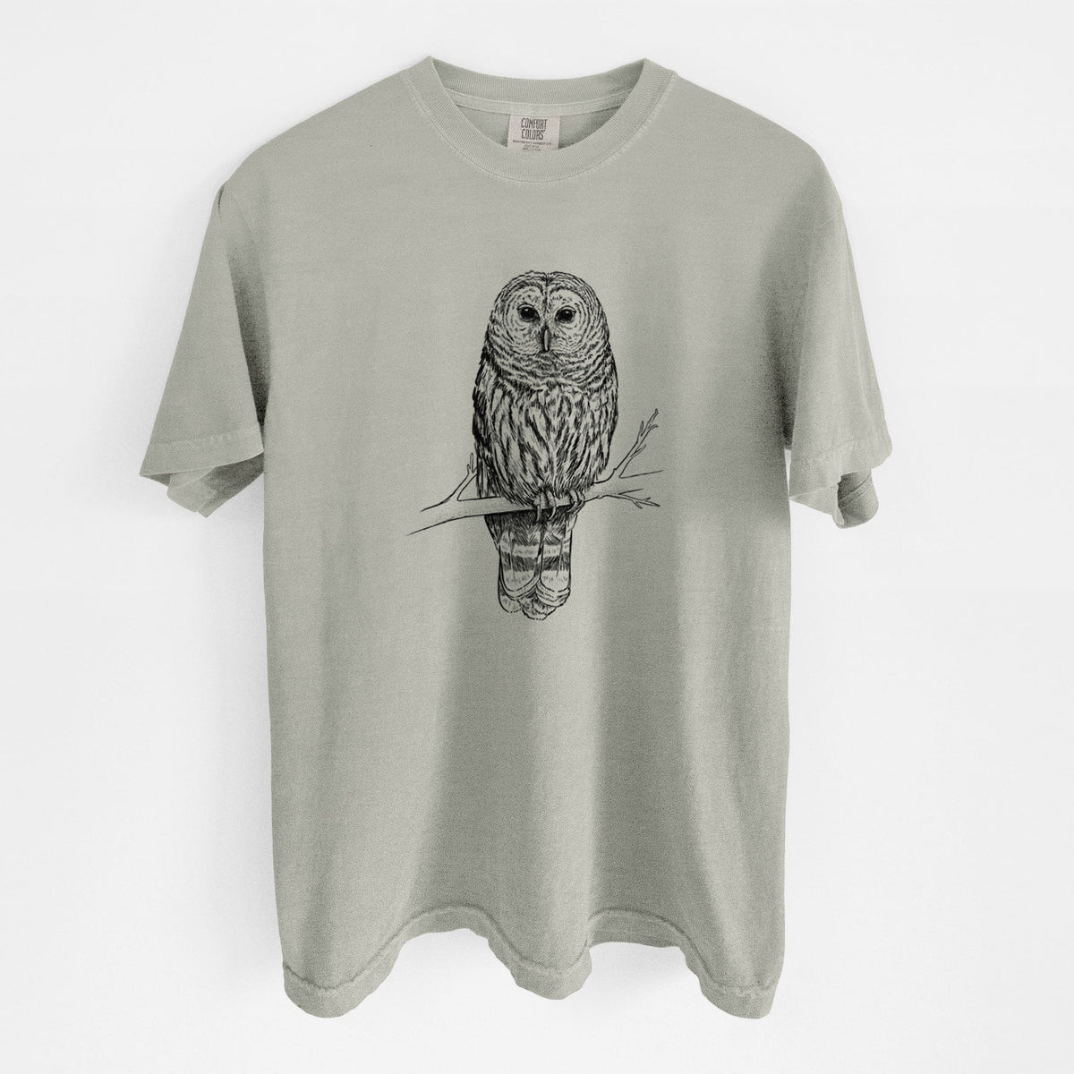 Sandstone beige Comfort Colors t-shirt laid flat, printed with a detailed black ink illustration of a barred owl perched on a branch.