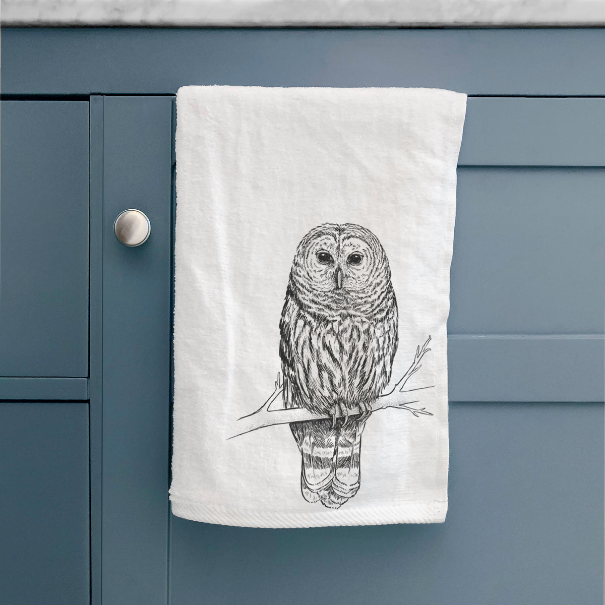 White hand towel printed with a detailed black ink illustration of a barred owl perched on a branch, hanging on a cabinet door.