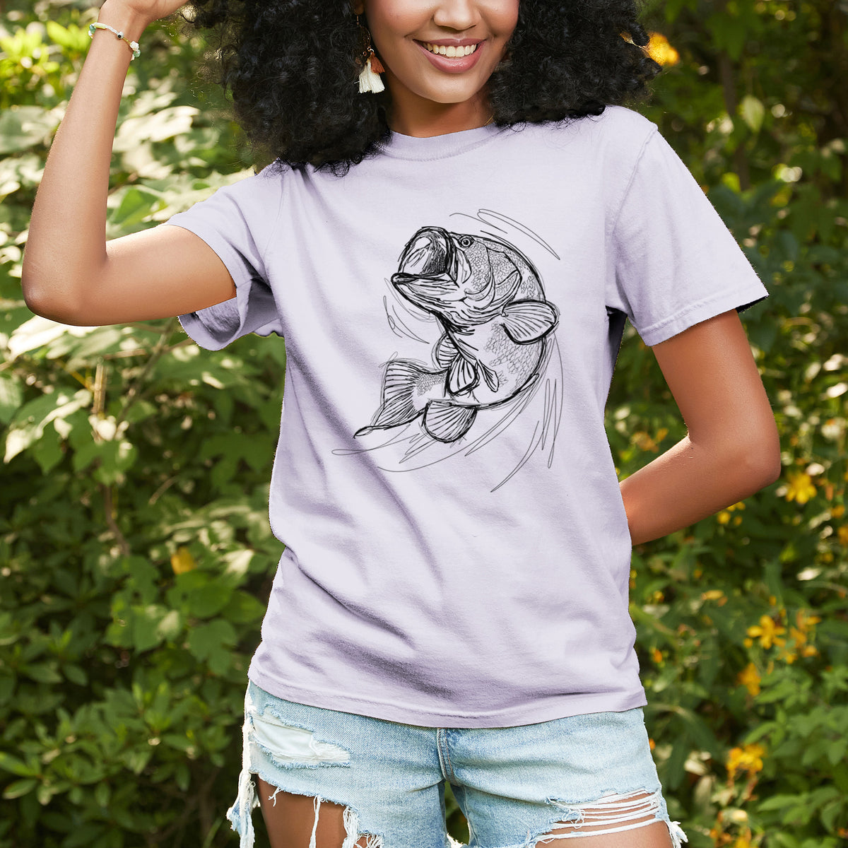 Woman wearing a Comfort Colors t-shirt printed with a detailed black ink illustration of a largemouth bass leaping with its mouth open, outdoors.
