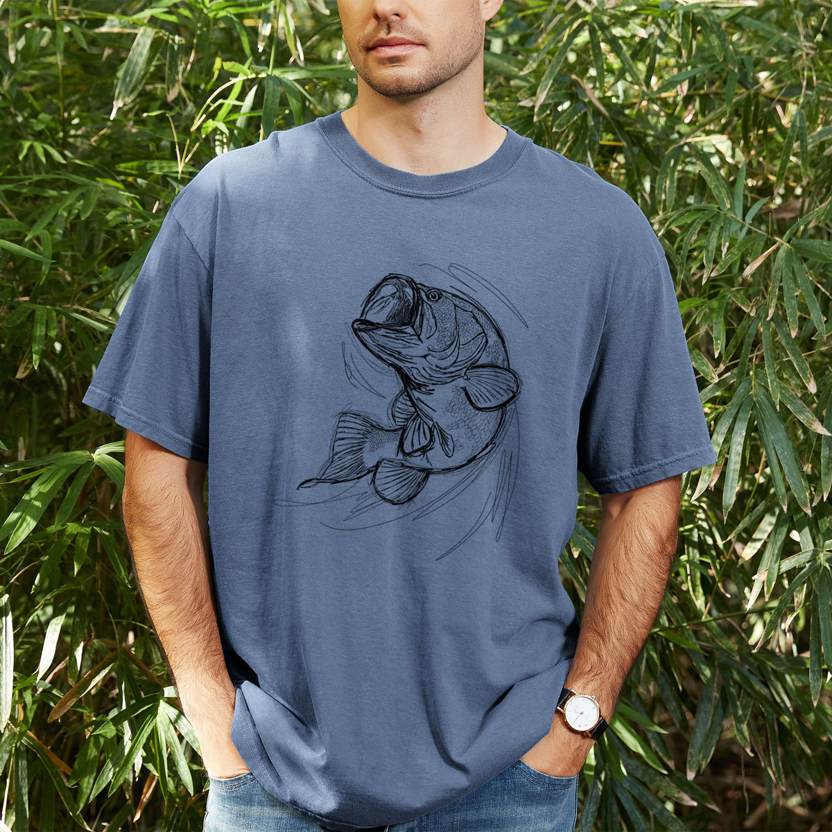 Man wearing a Comfort Colors t-shirt printed with a detailed black ink illustration of a largemouth bass leaping with its mouth open, outdoors.
