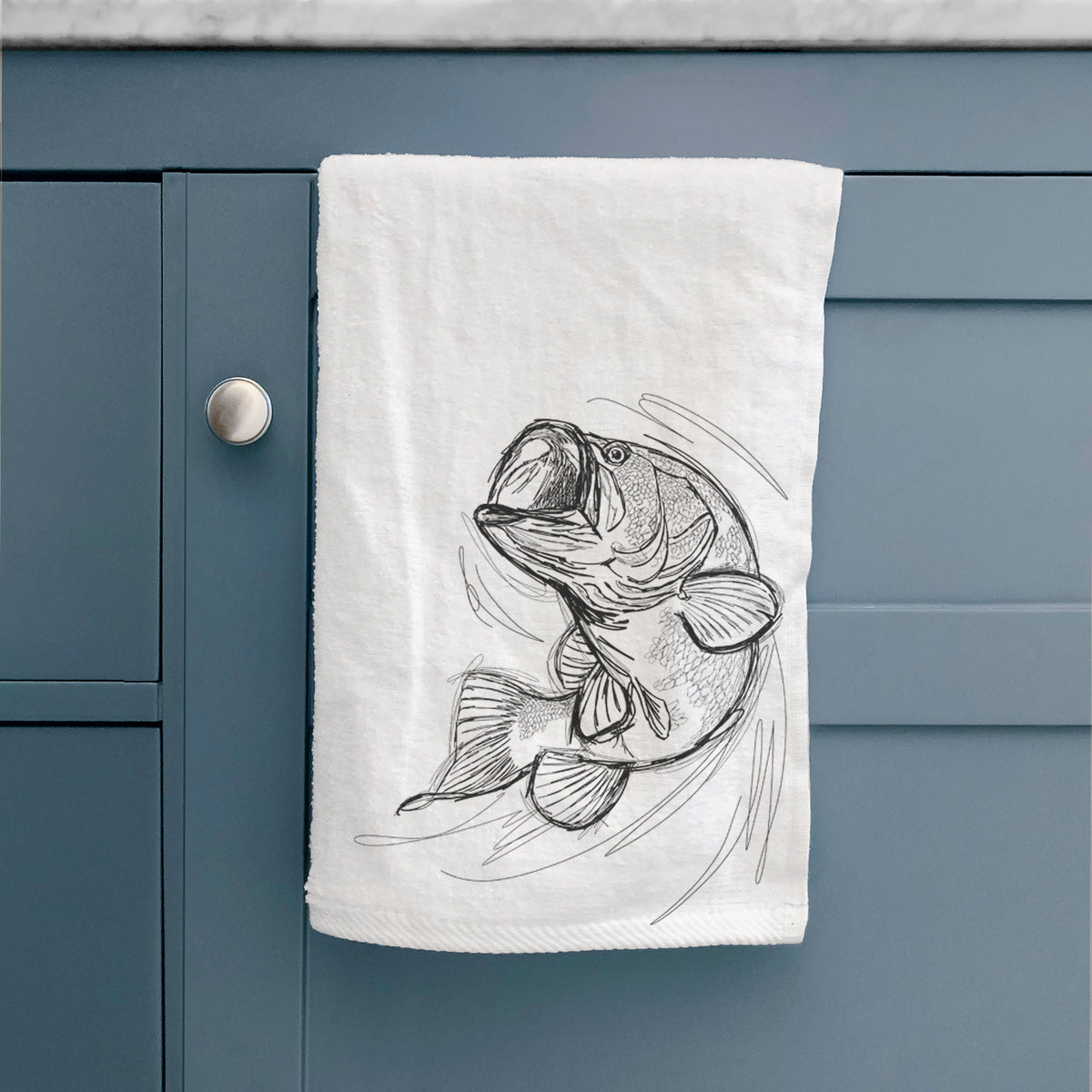 White hand towel printed with a detailed black ink illustration of a largemouth bass leaping with its mouth open, hanging on a cabinet door.