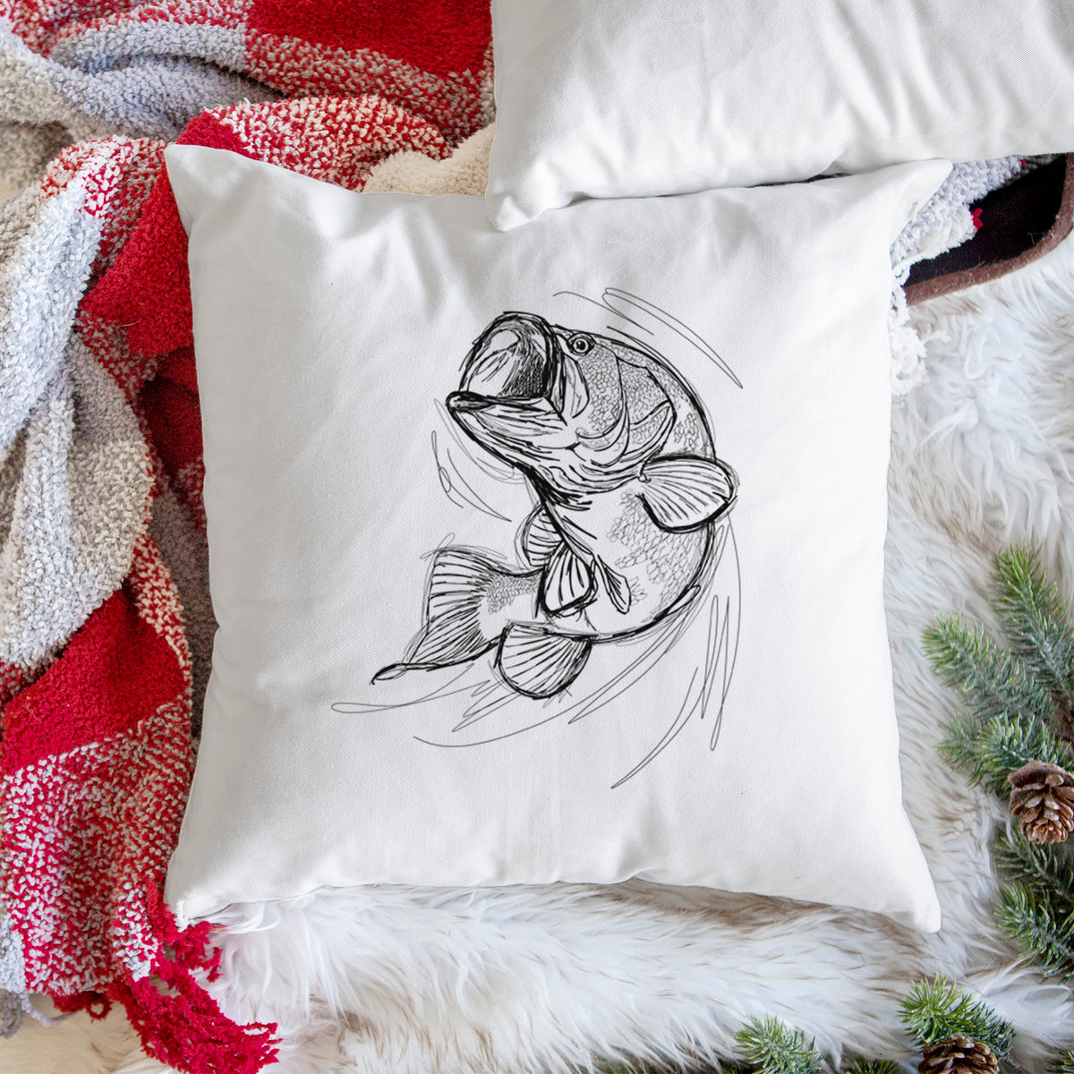 White pillow cover printed with a detailed black ink illustration of a largemouth bass leaping with its mouth open, on a woven chair.