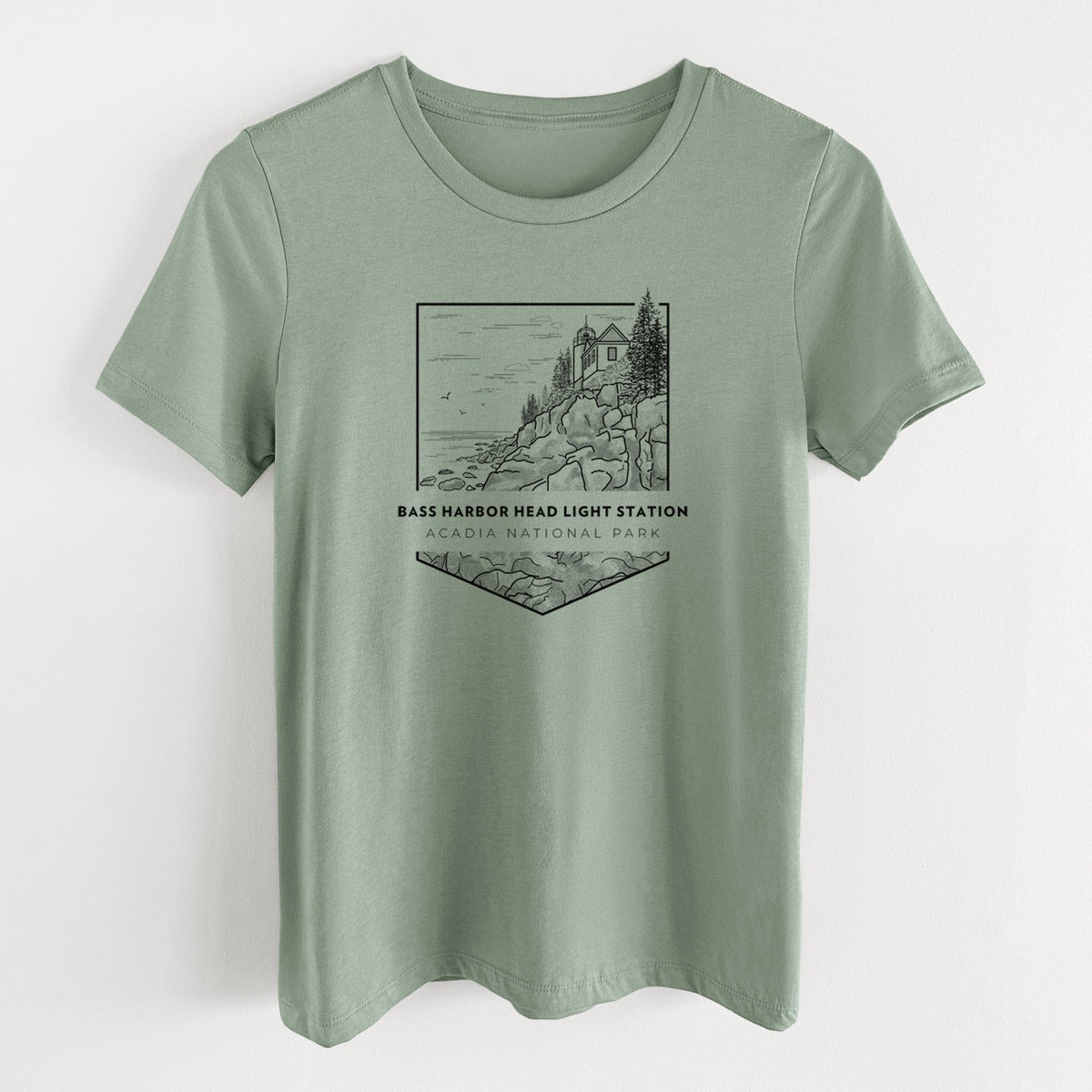 Sage green women's relaxed fit cotton t-shirt laid flat, printed with a black line art badge of Bass Harbor Head Light Station on a rocky cliff, with the words Acadia National Park.