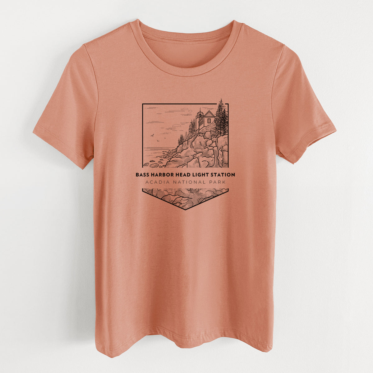 Terracotta orange women's relaxed fit cotton t-shirt laid flat, printed with a black line art badge of Bass Harbor Head Light Station on a rocky cliff, with the words Acadia National Park.
