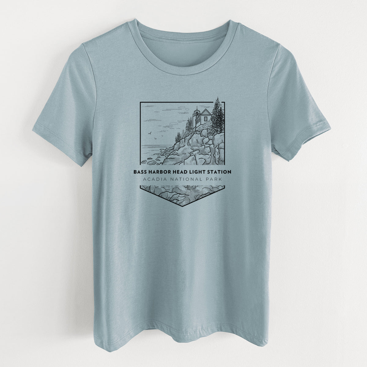 Vintage denim women's relaxed fit cotton t-shirt laid flat, printed with a black line art badge of Bass Harbor Head Light Station on a rocky cliff, with the words Acadia National Park.