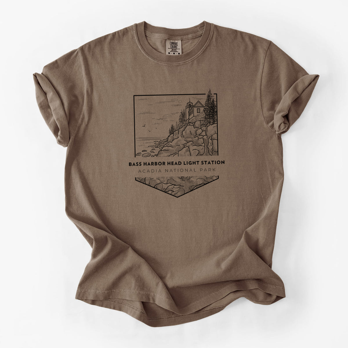 Espresso brown Comfort Colors t-shirt laid flat, printed with a black line art badge of Bass Harbor Head Light Station on a rocky cliff, with the words Acadia National Park.