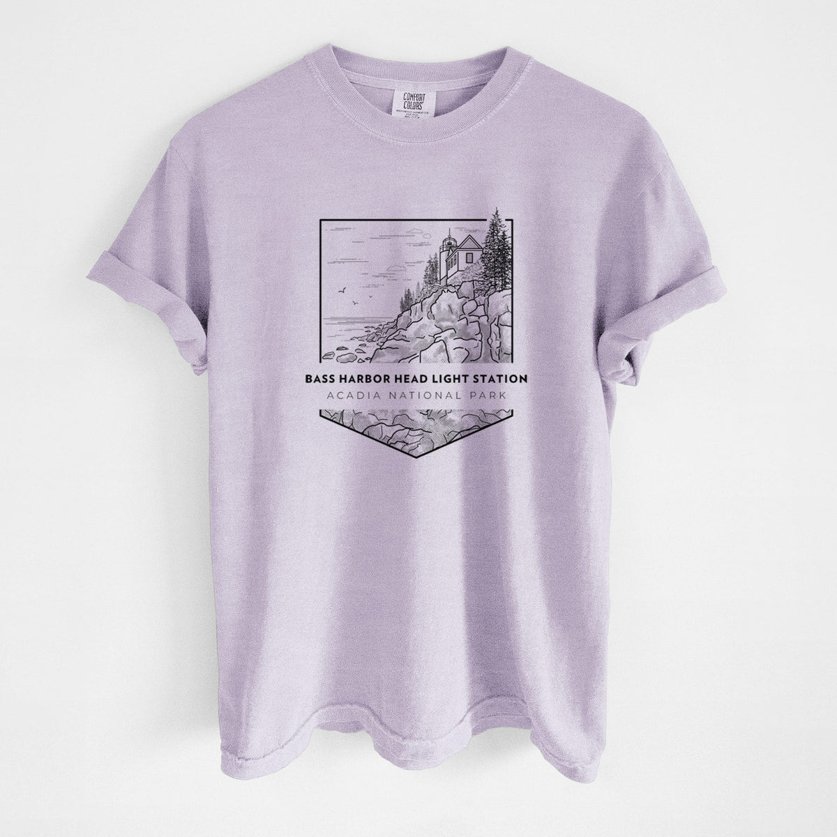 Orchid purple Comfort Colors t-shirt laid flat, printed with a black line art badge of Bass Harbor Head Light Station on a rocky cliff, with the words Acadia National Park.