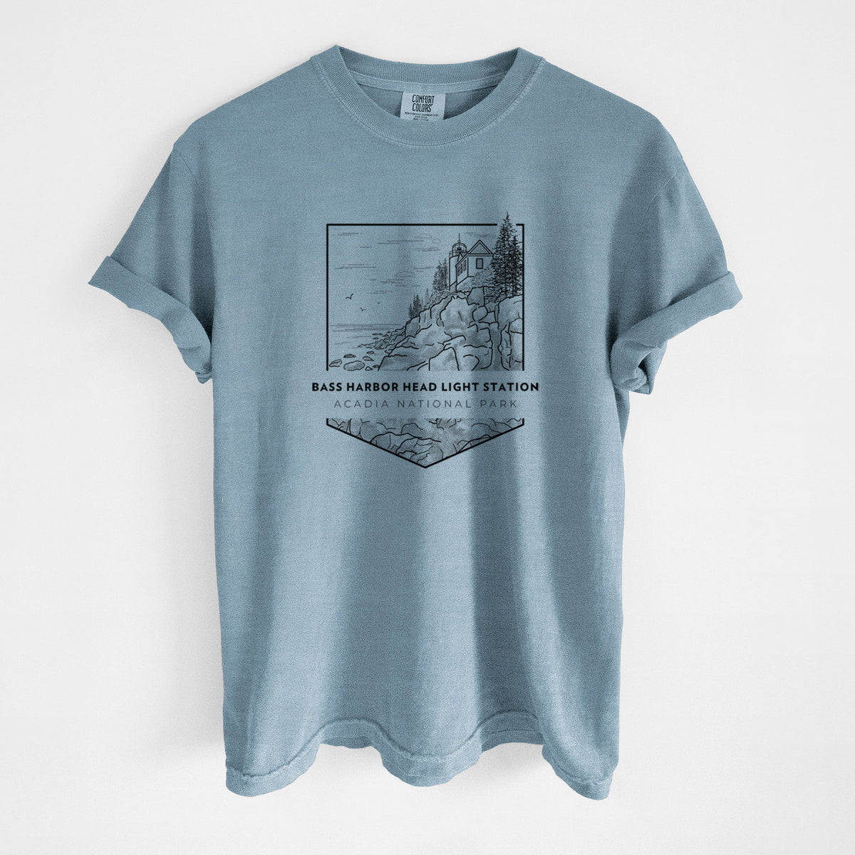 Steel blue Comfort Colors t-shirt laid flat, printed with a black line art badge of Bass Harbor Head Light Station on a rocky cliff, with the words Acadia National Park.