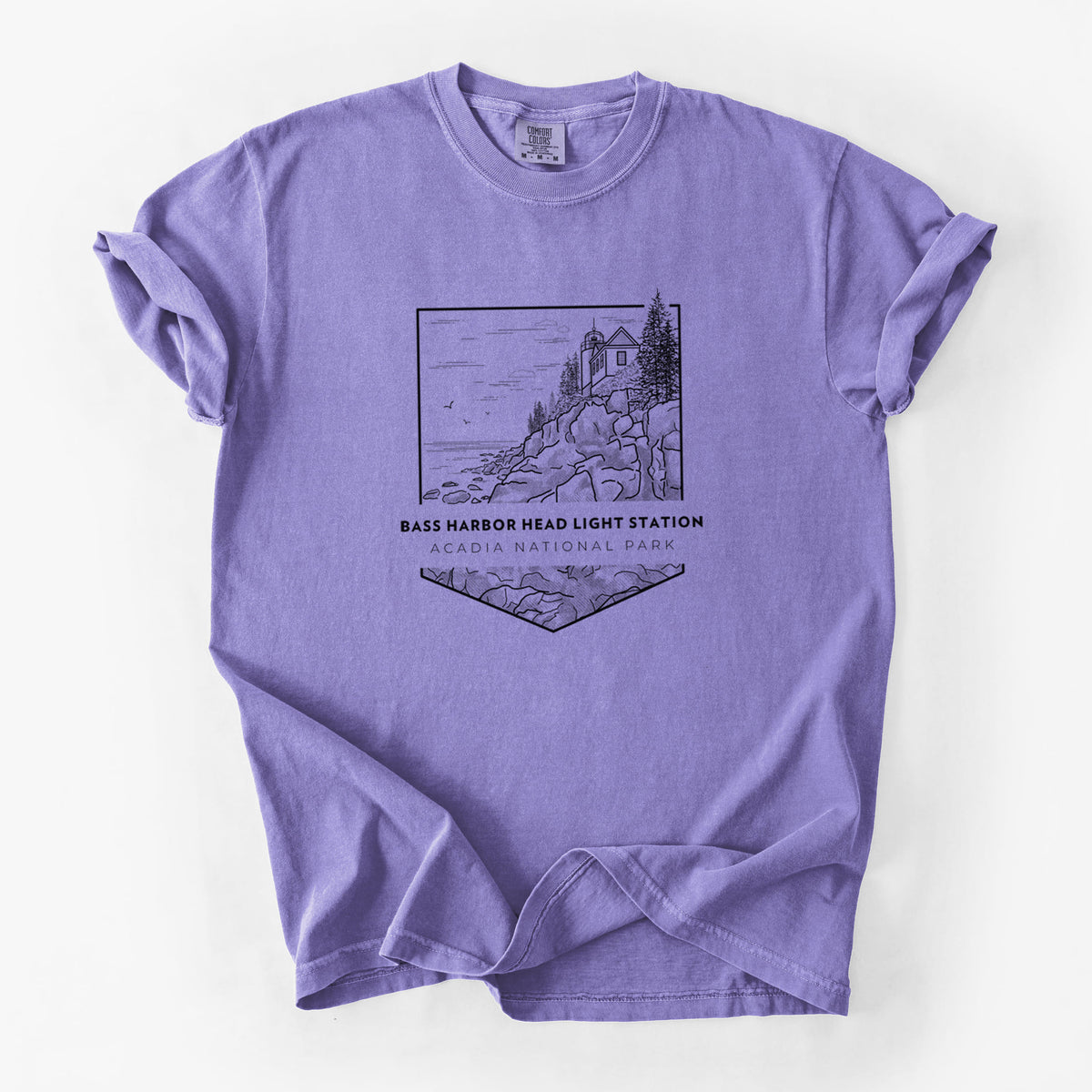 Violet purple Comfort Colors t-shirt laid flat, printed with a black line art badge of Bass Harbor Head Light Station on a rocky cliff, with the words Acadia National Park.