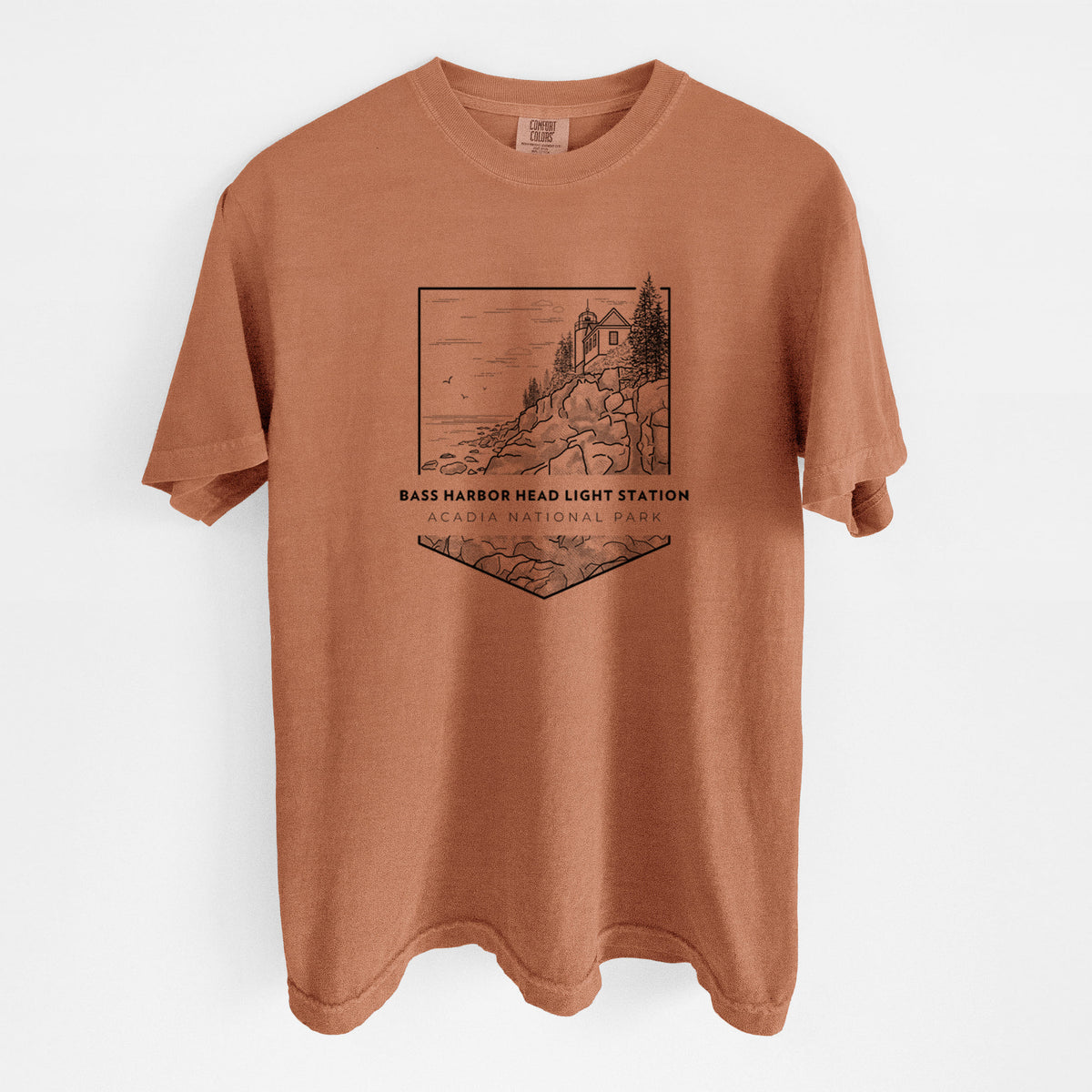 Yam burnt orange Comfort Colors t-shirt laid flat, printed with a black line art badge of Bass Harbor Head Light Station on a rocky cliff, with the words Acadia National Park.