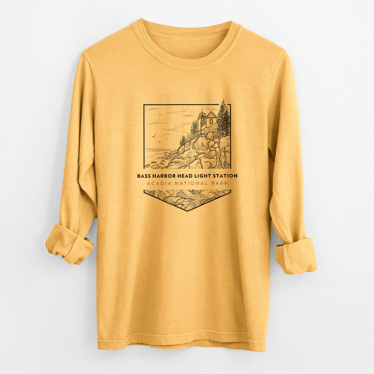 Golden wheat yellow Comfort Colors long sleeve shirt laid flat with the cuffs rolled, printed with a black line art badge of Bass Harbor Head Light Station on a rocky cliff, with the words Acadia National Park.