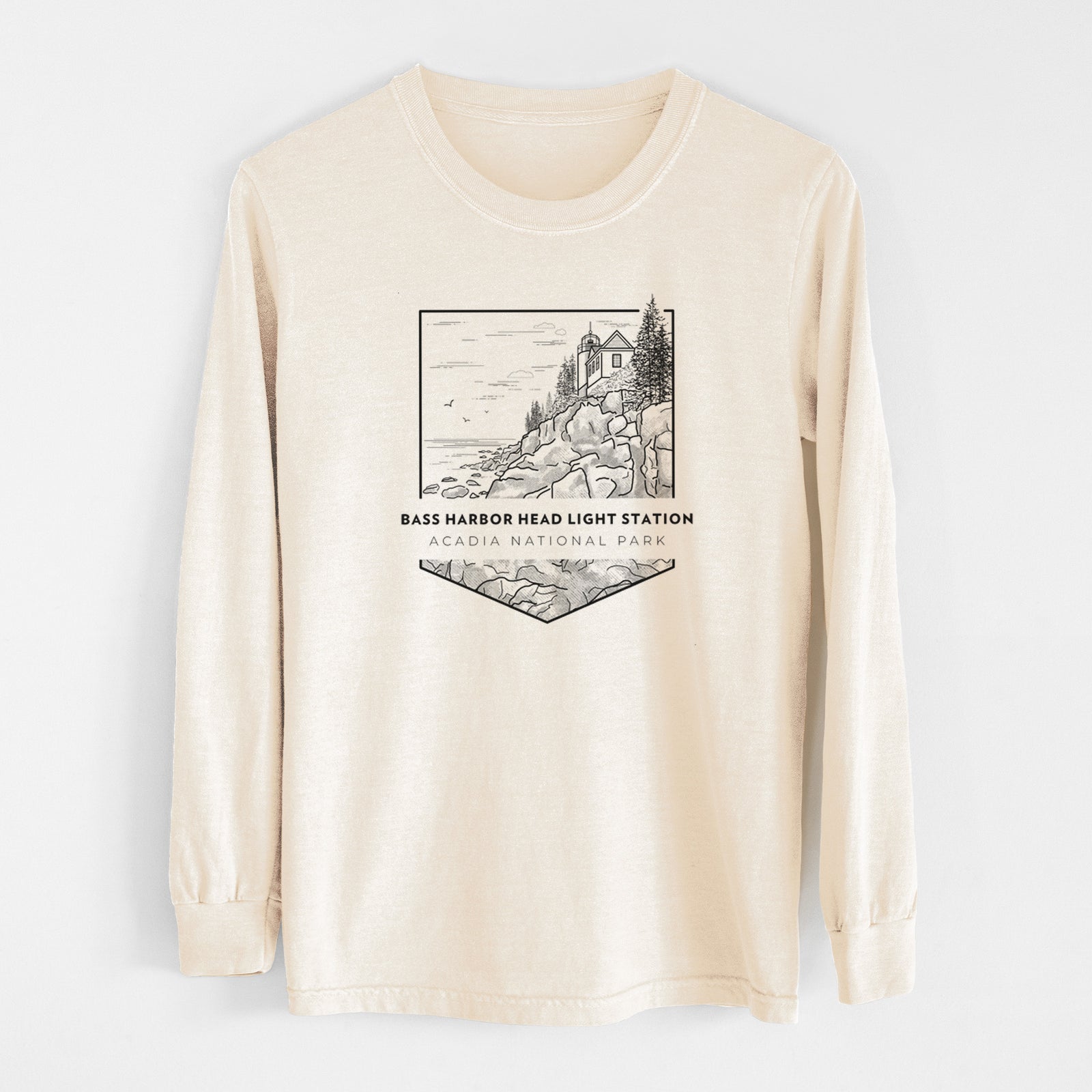 Ivory Comfort Colors long sleeve shirt laid flat, printed with a black line art badge of Bass Harbor Head Light Station on a rocky cliff, with the words Acadia National Park.