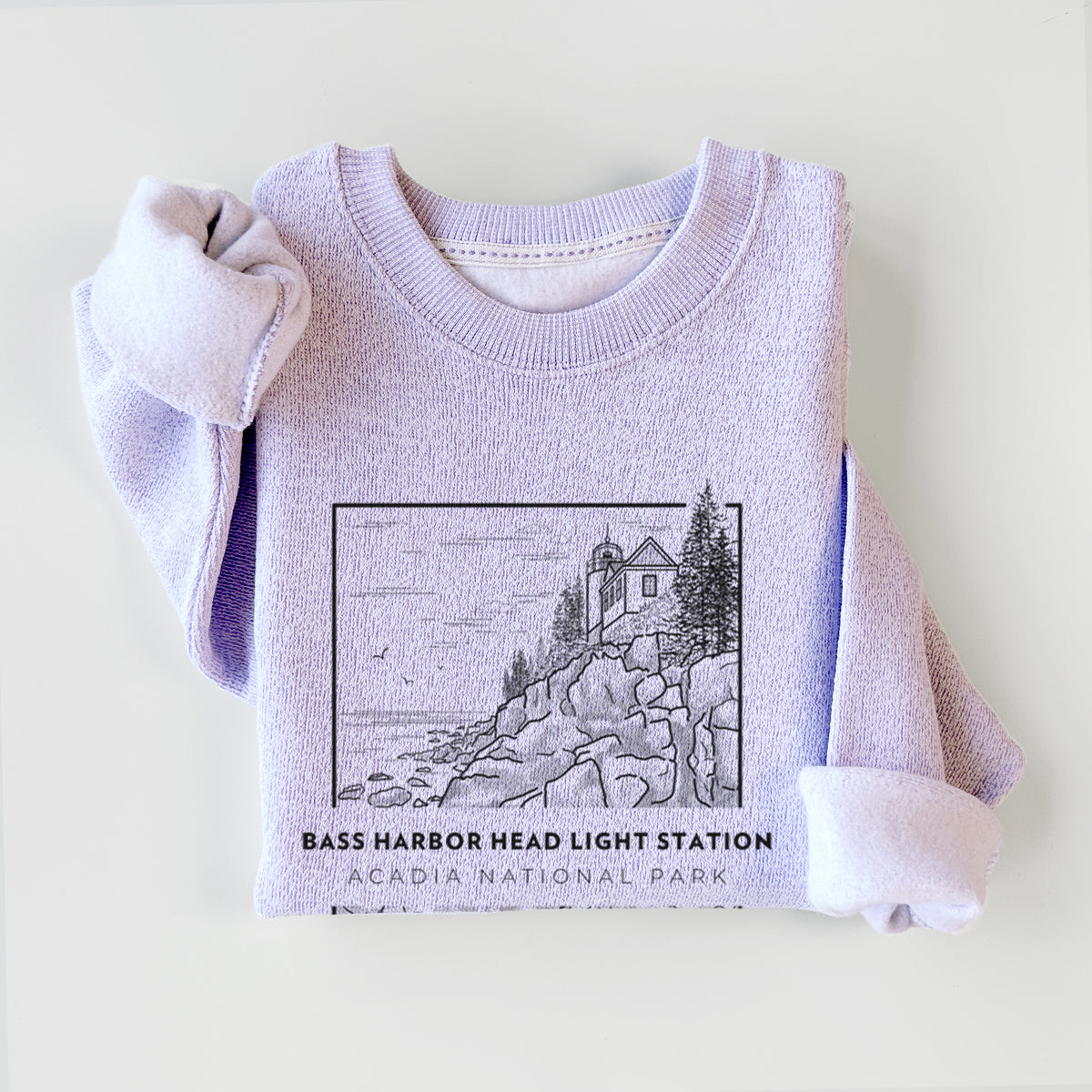 Ice purple knit sweatshirt printed with a black line art badge of Bass Harbor Head Light Station on a rocky cliff, with the words Acadia National Park, styled flat.