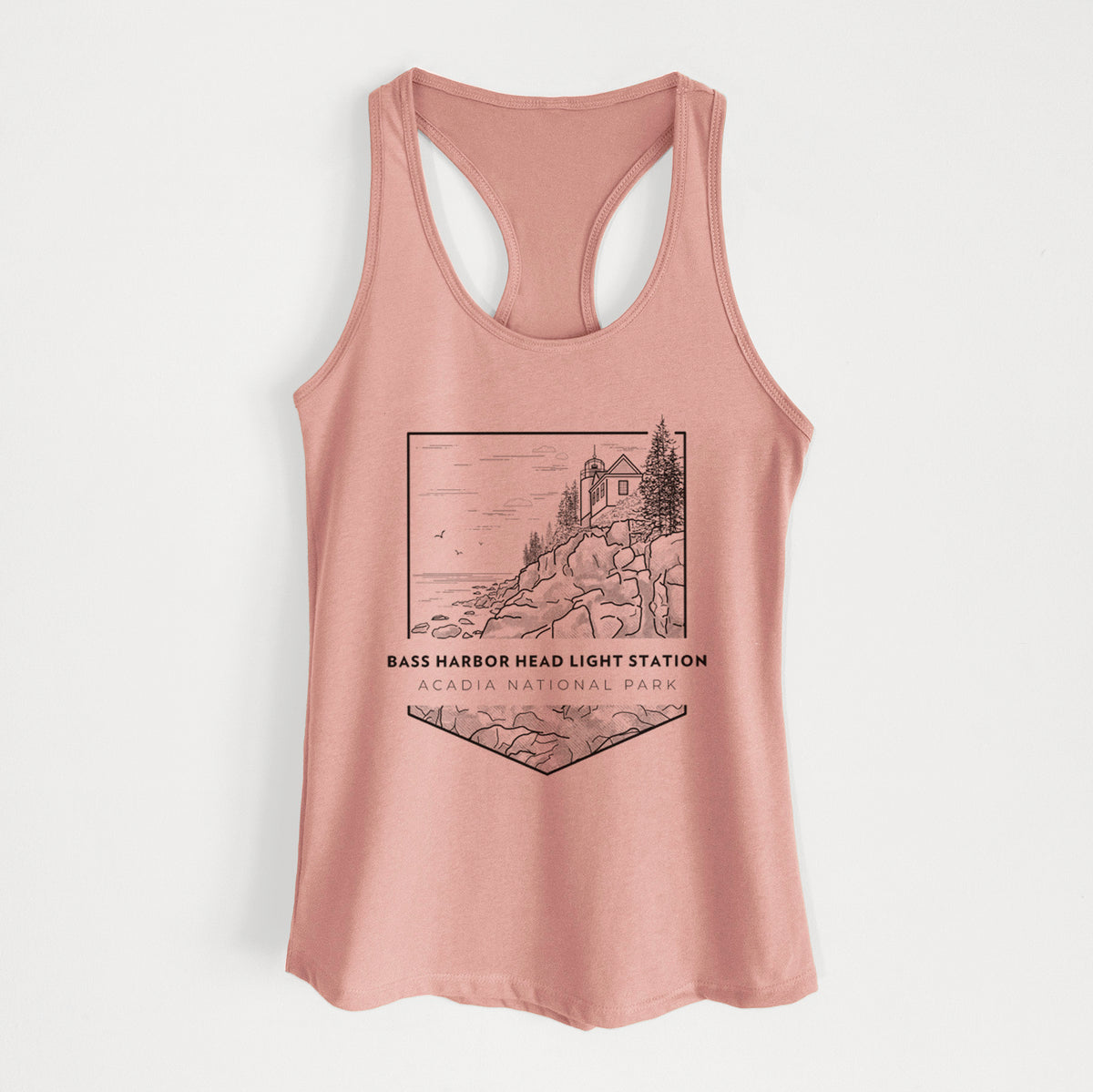 Desert pink women's racerback tank top laid flat, printed with a black line art badge of Bass Harbor Head Light Station on a rocky cliff, with the words Acadia National Park.