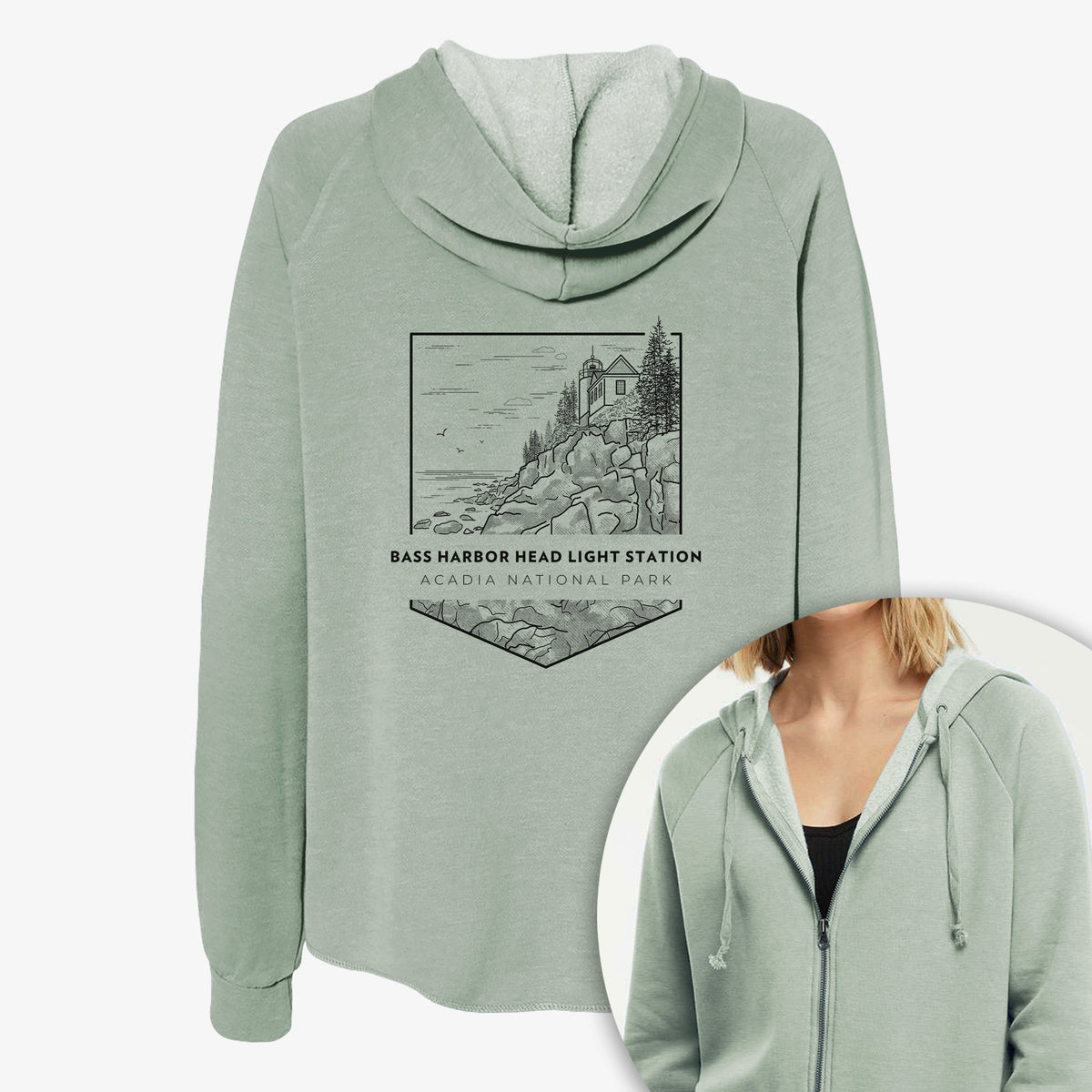 Women's Cali Wave zip-up sweatshirt printed with a black line art badge of Bass Harbor Head Light Station on a rocky cliff, with the words Acadia National Park, with a close-up of the zipper.