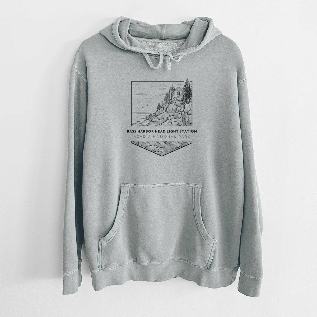 Sage green pigment dyed hoodie laid flat, printed with a black line art badge of Bass Harbor Head Light Station on a rocky cliff, with the words Acadia National Park.