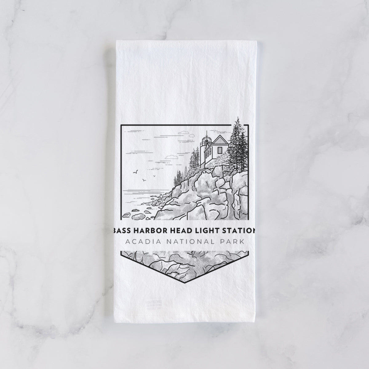 White cotton tea towel laid flat on marble, printed with a black line art badge of Bass Harbor Head Light Station on a rocky cliff, with the words Acadia National Park.