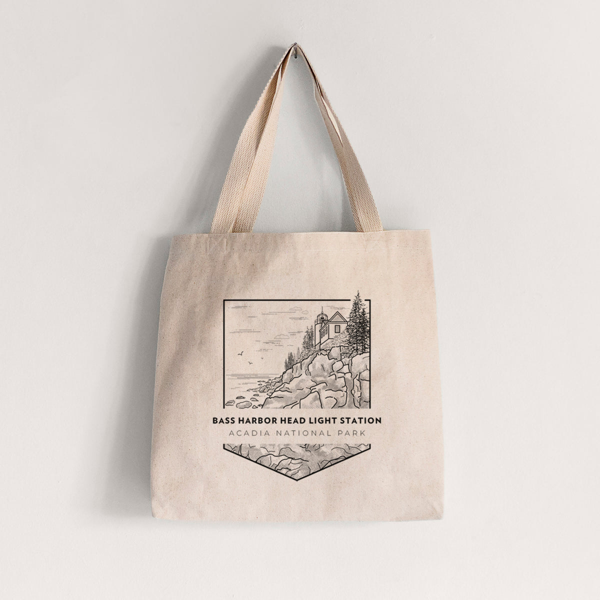 Natural canvas tote bag printed with a black line art badge of Bass Harbor Head Light Station on a rocky cliff, with the words Acadia National Park.