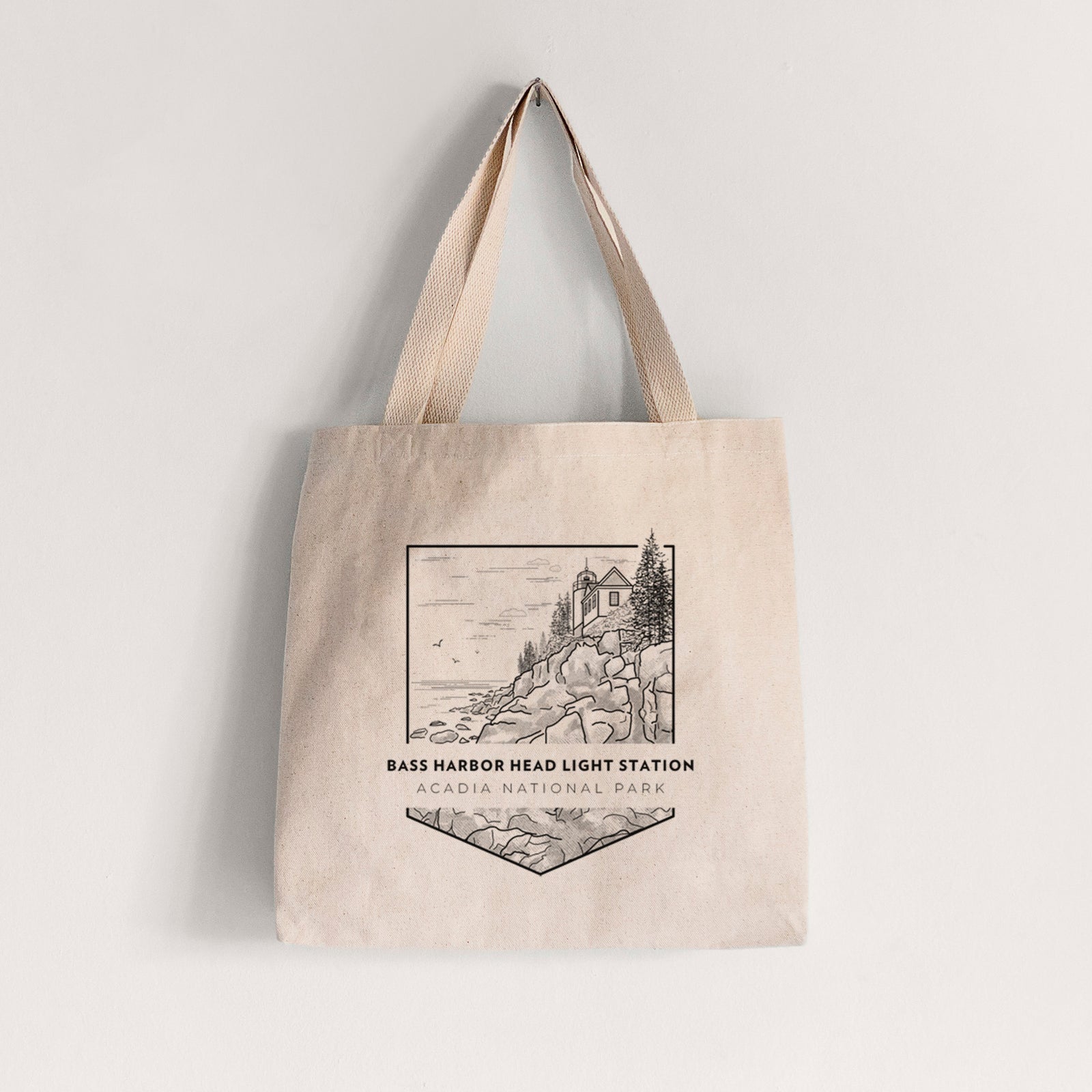 Natural canvas tote bag printed with a black line art badge of Bass Harbor Head Light Station on a rocky cliff, with the words Acadia National Park.