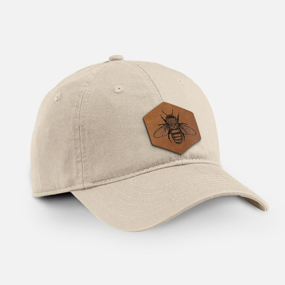 Stone cotton baseball hat with a brown leather hexagon patch engraved with a honey bee on the front.