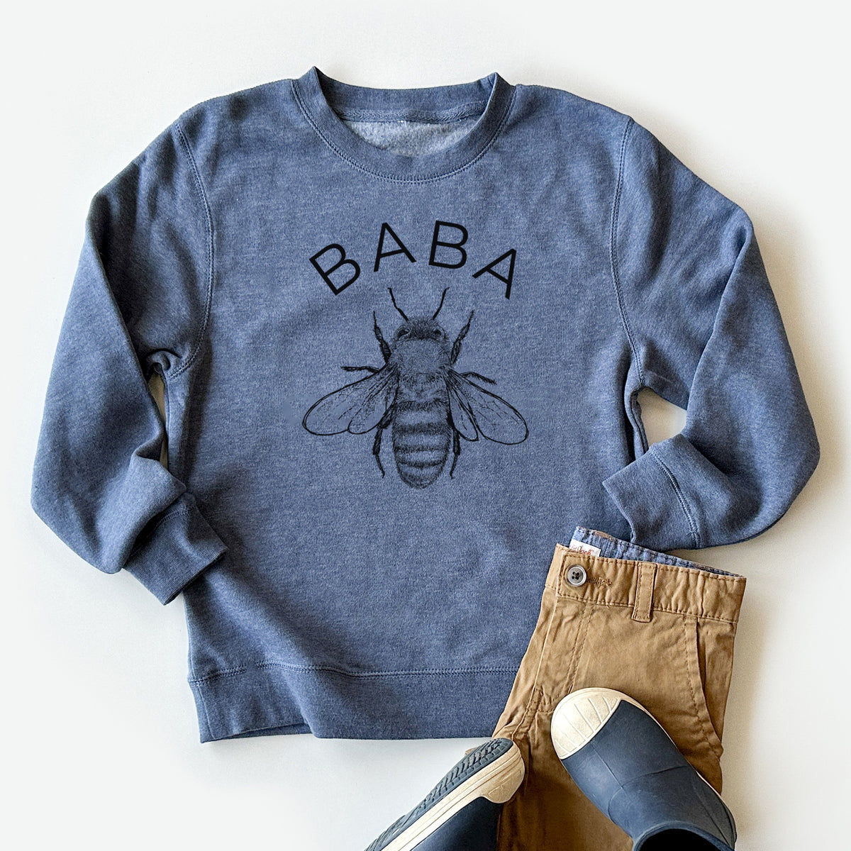 Youth crewneck sweatshirt printed with a black ink honey bee beneath the word Baba, styled flat with khaki pants and shoes.