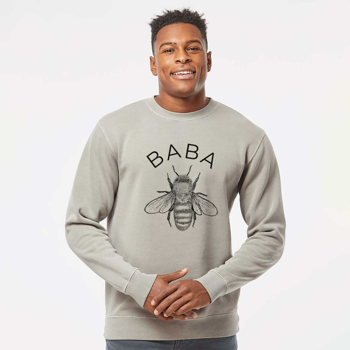 Model wearing a cement grey pigment dyed crewneck sweatshirt printed with a black ink honey bee beneath the word Baba.