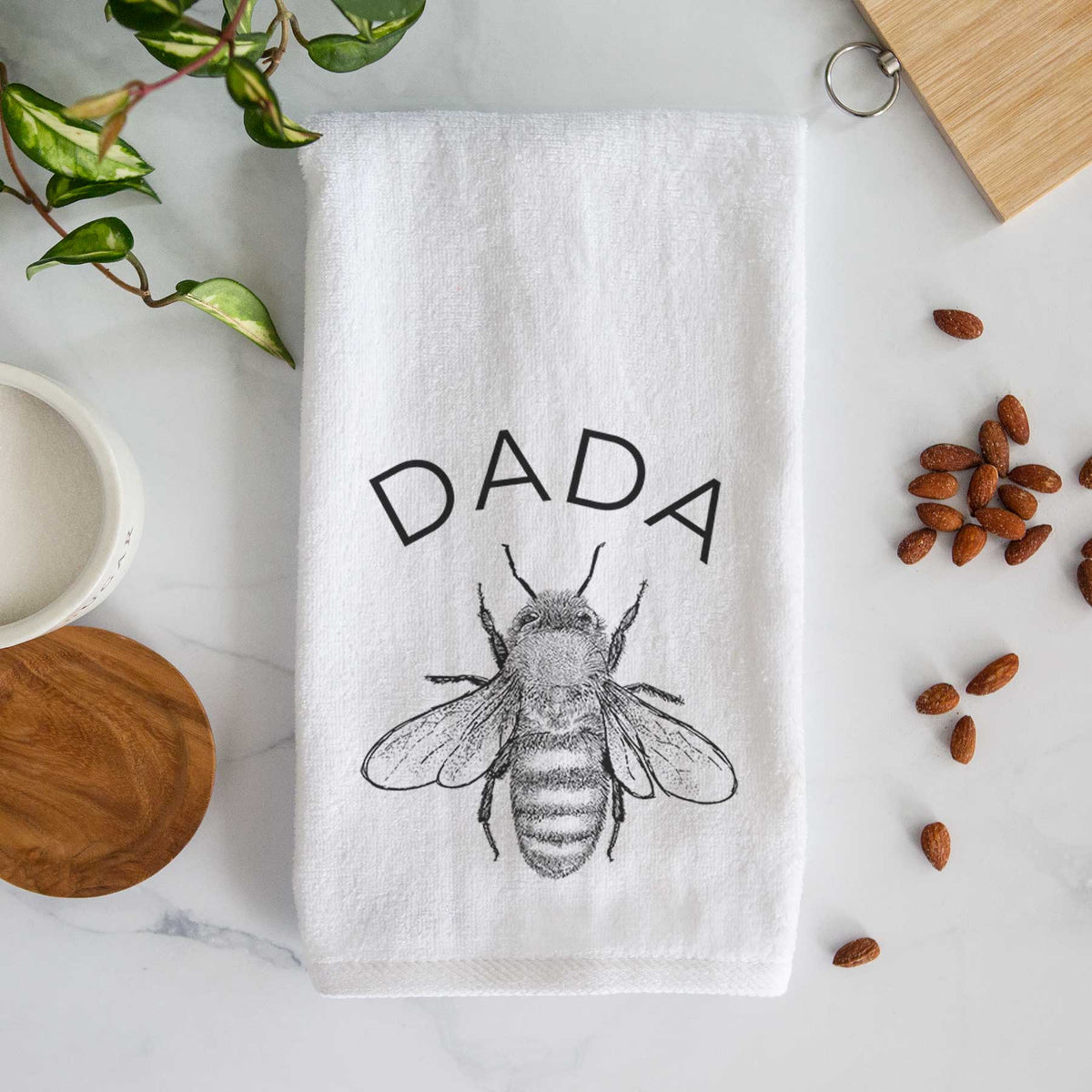 White hand towel printed with a black ink honey bee beneath the word Dada.