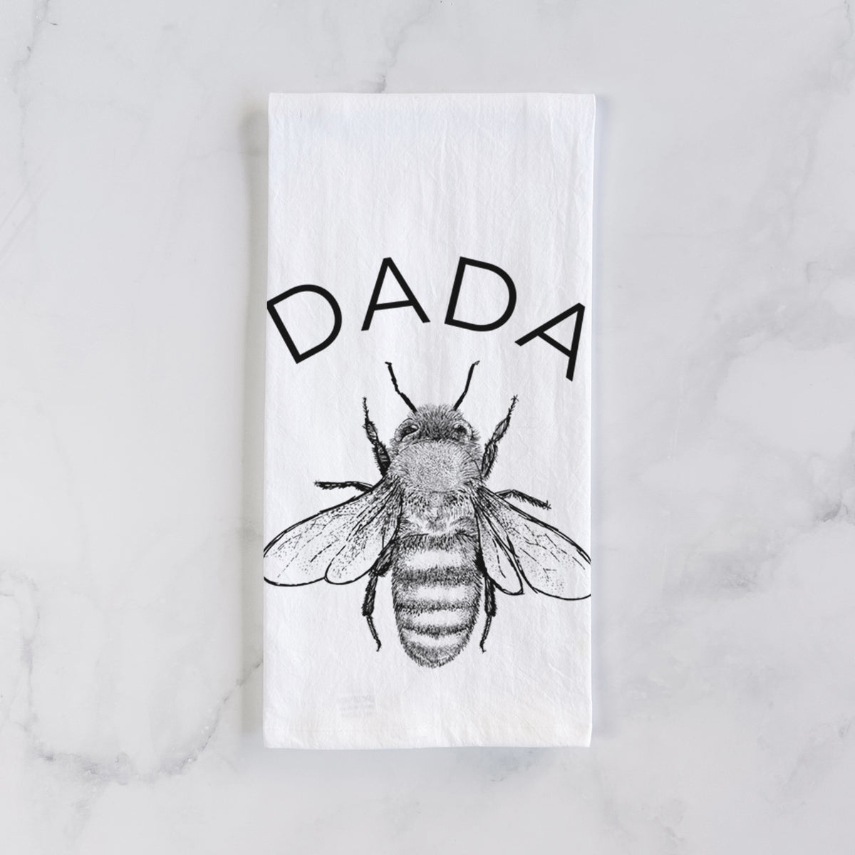 White cotton tea towel laid flat on marble, printed with a black ink honey bee beneath the word Dada.