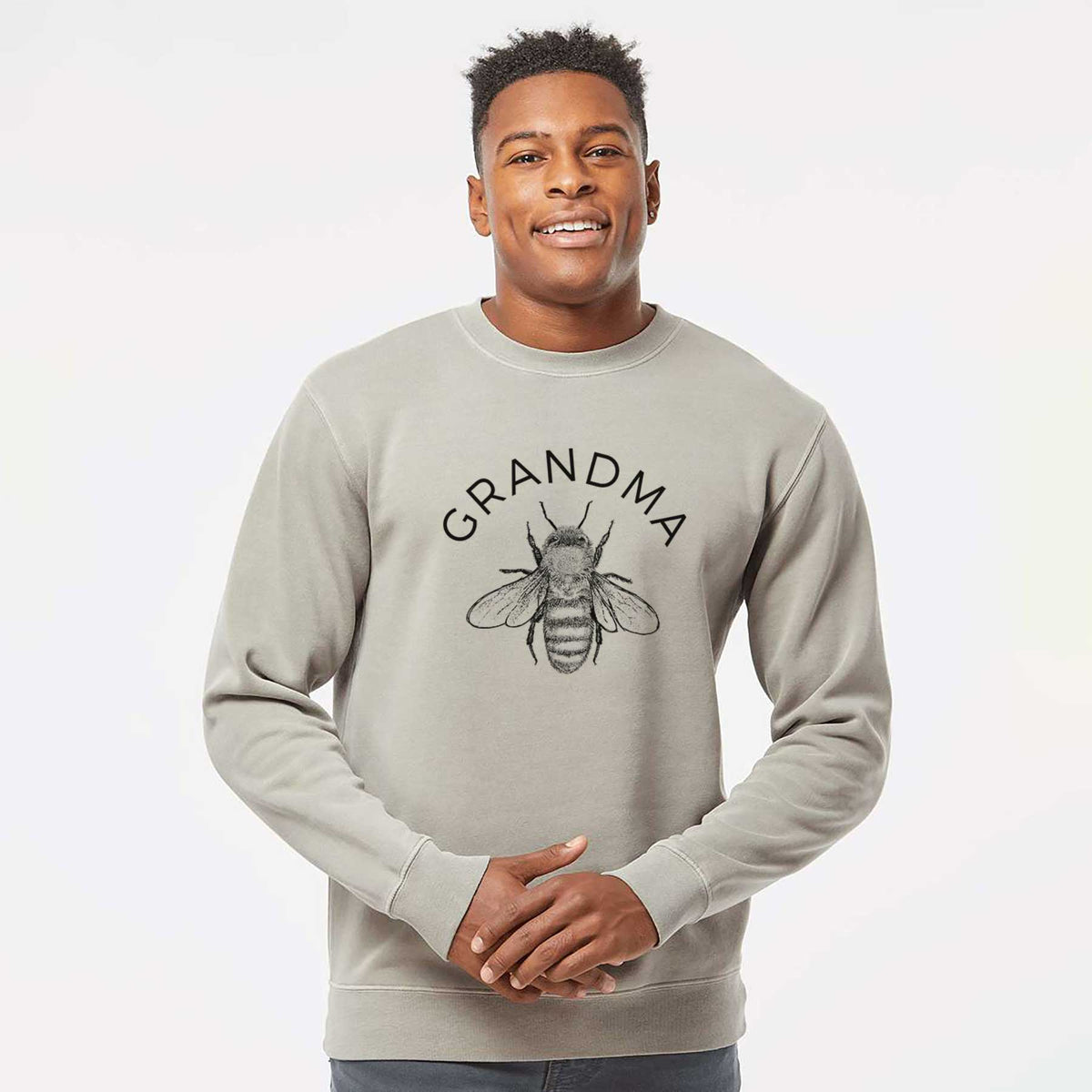 Model wearing a cement grey pigment dyed crewneck sweatshirt printed with a black ink honey bee beneath the word Grandma.