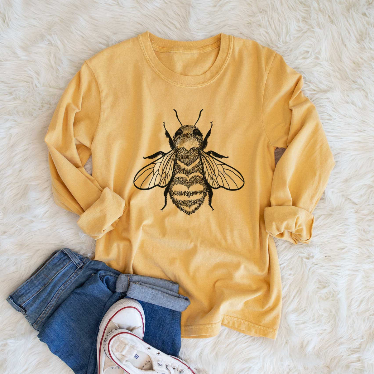 Golden wheat yellow Comfort Colors long sleeve shirt printed with a black ink bee with a heart pattern on its body, shown in a lifestyle photo.