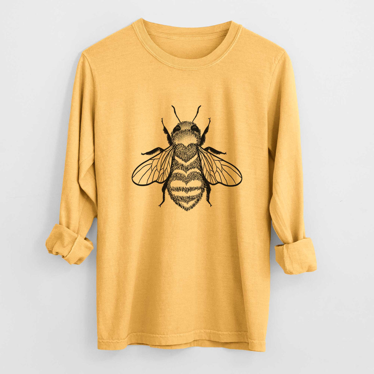 Golden wheat yellow Comfort Colors long sleeve shirt laid flat with the cuffs rolled, printed with a black ink bee with a heart pattern on its body.