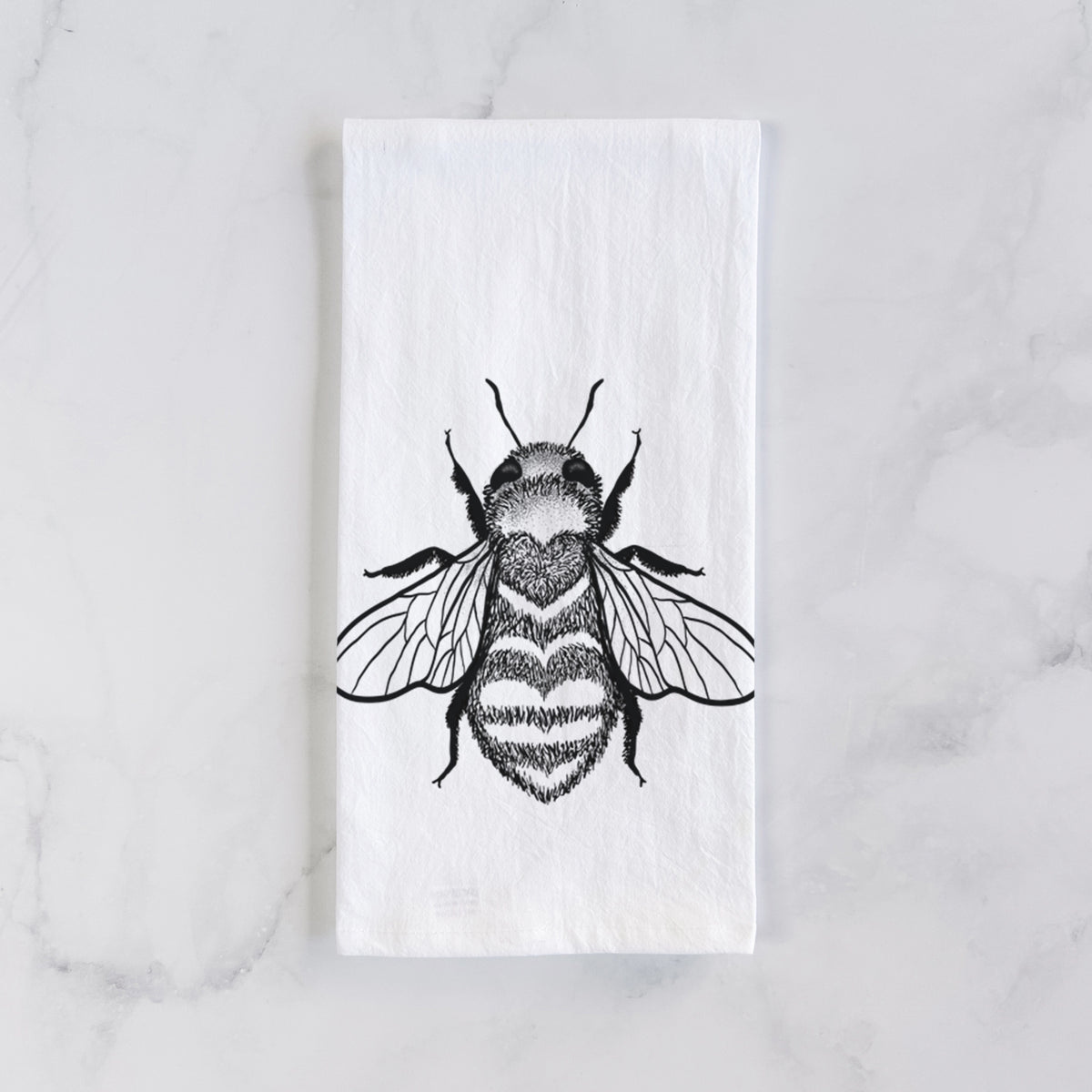 White cotton tea towel laid flat on marble, printed with a black ink bee with a heart pattern on its body.