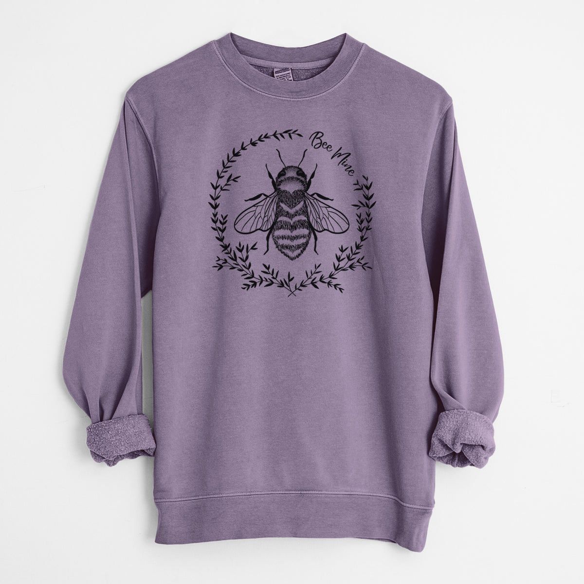 Plum purple pigment dyed crewneck sweatshirt laid flat with the sleeves rolled, printed with a black ink bee inside a wreath of leaves with the words Bee Mine.