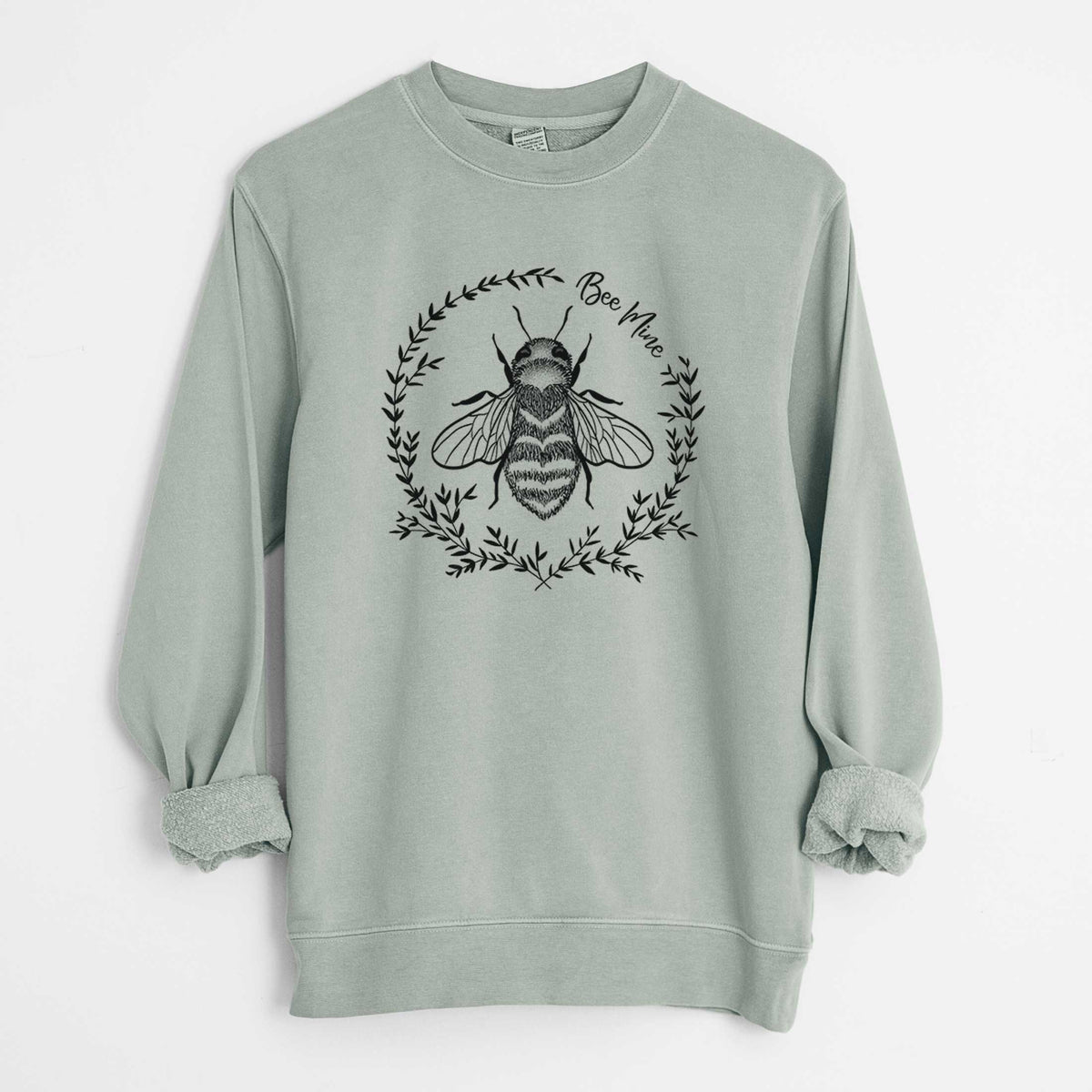 Sage green pigment dyed crewneck sweatshirt laid flat with the sleeves rolled, printed with a black ink bee inside a wreath of leaves with the words Bee Mine.