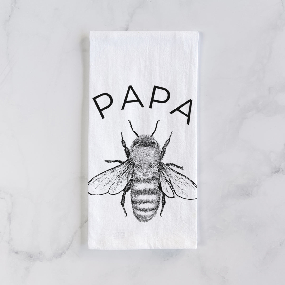 White cotton tea towel laid flat on marble, printed with a black ink honey bee beneath the word Papa.